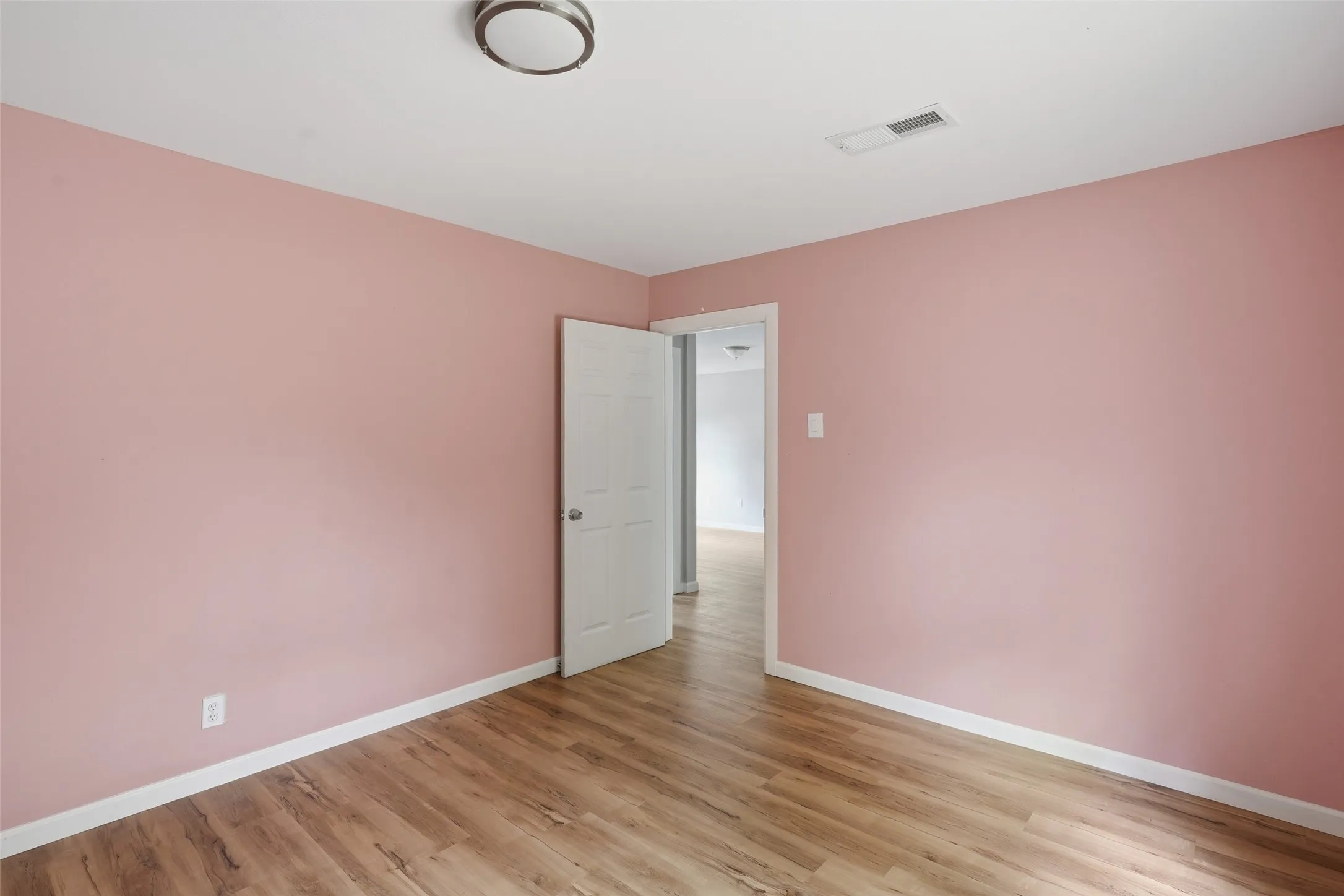 Bright secondary bedroom featuring soft pink walls, white crown molding, wood-finish flooring, and dual closet access with mirrored sliding doors