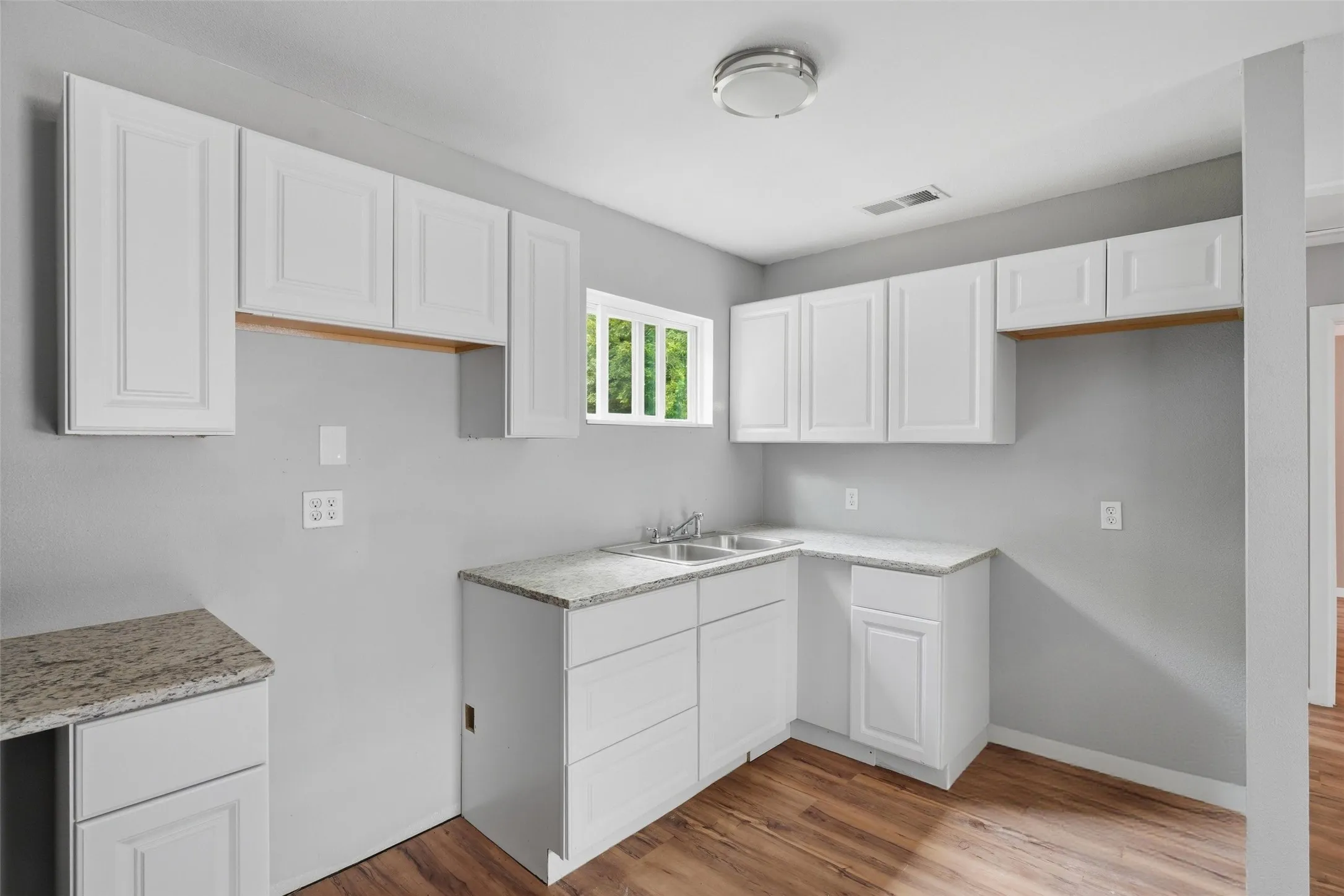 Bright kitchen featuring white shaker-style cabinetry with wood-tone accents, laminate countertops, and a single-basin sink with faucet