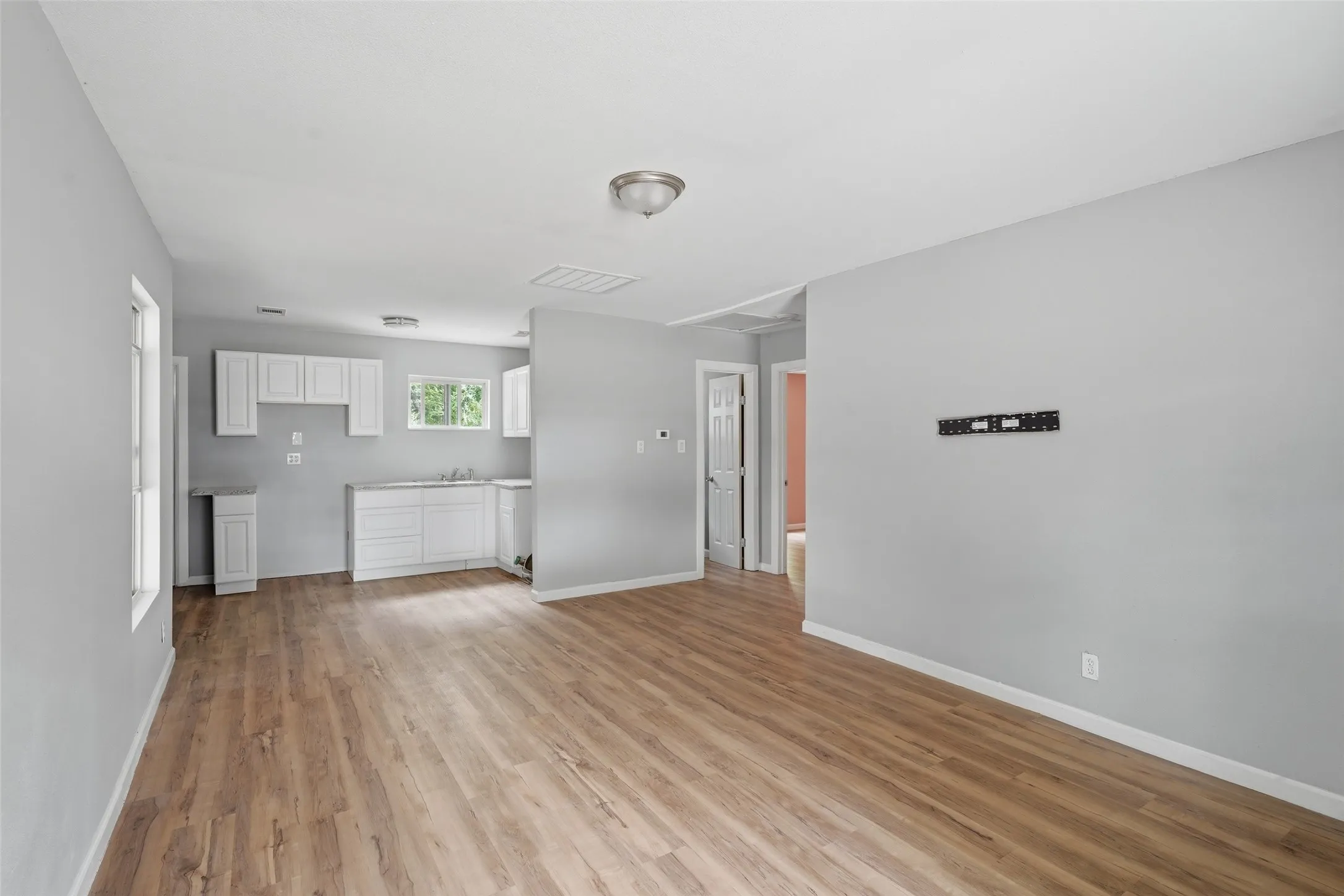 Open-concept living area with warm wood-finish flooring throughout, white cabinetry, and stainless steel appliances