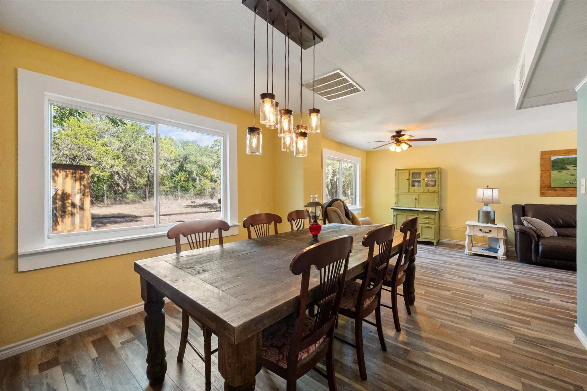 Open-concept living area featuring wood-finish flooring, ample natural light from large windows, and a multi-bulb linear pendant light fixture