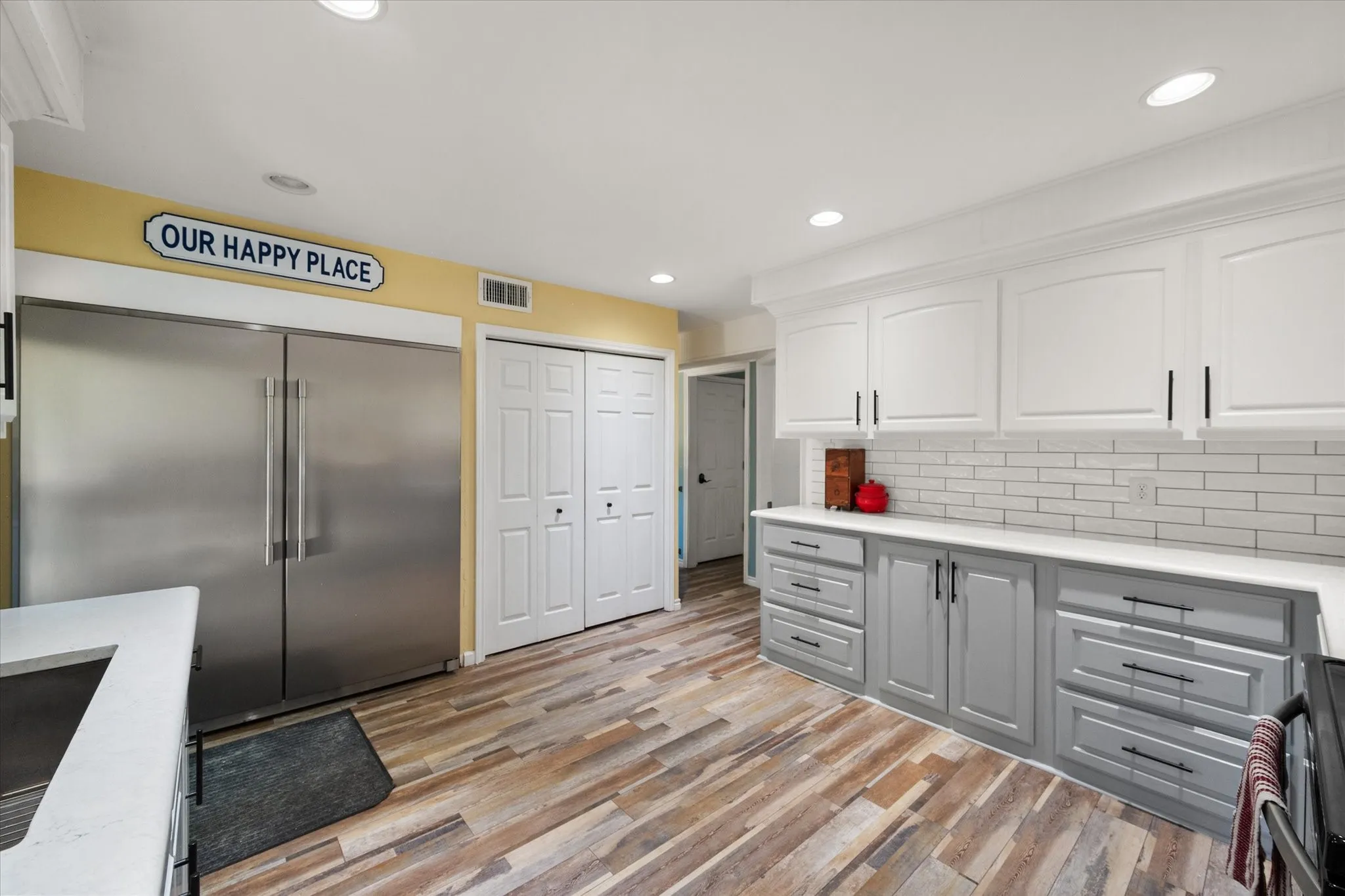 White upper cabinetry with contrasting gray base cabinetry, light-toned countertops, subway tile backsplash, and wood-finish flooring