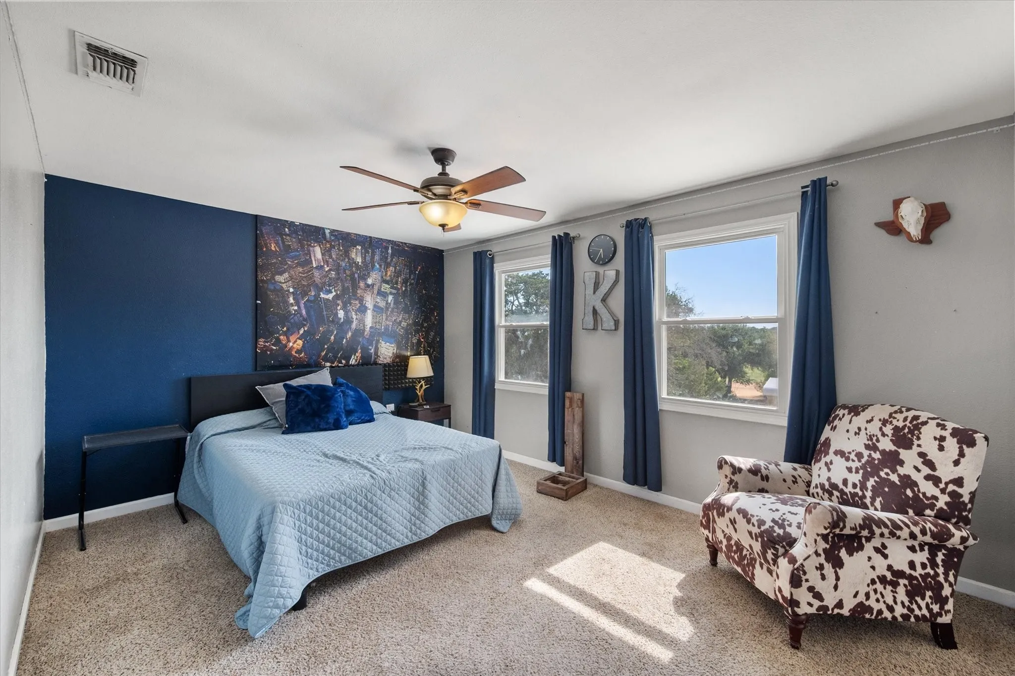 Carpeted room featuring a ceiling fan with integrated lighting, two windows, and a dark accent wall