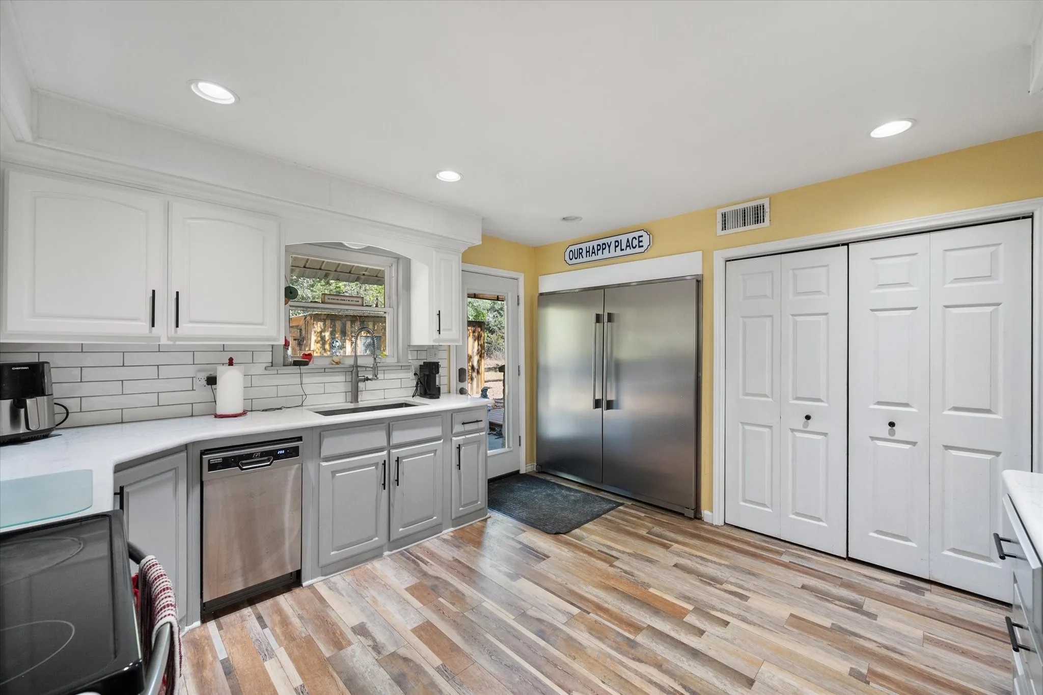 Kitchen featuring wood-finish flooring, white subway tile backsplash, white upper cabinetry, grey lower cabinetry, and stainless steel appliances