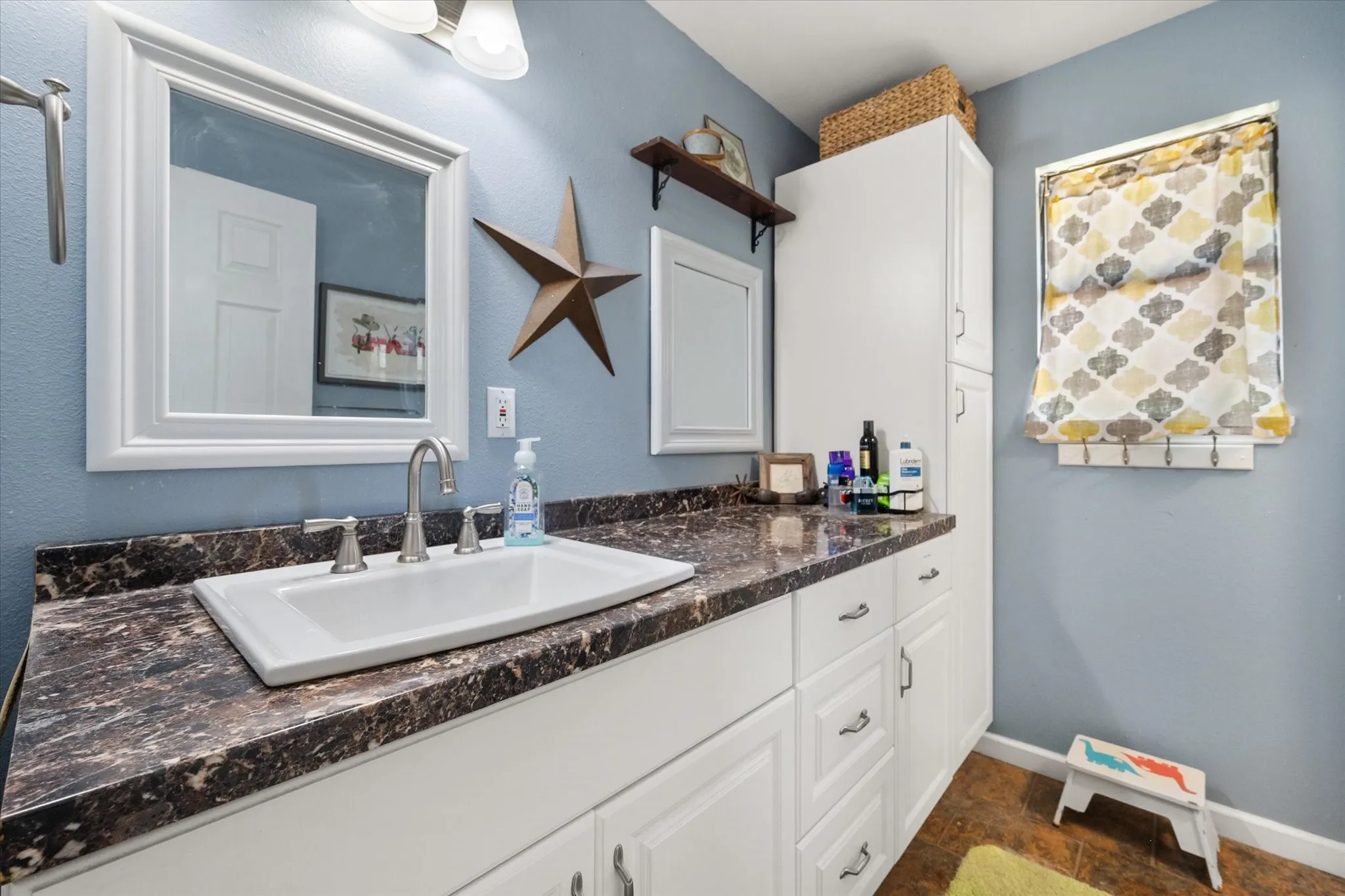 White vanity with a drop-in sink, dark speckled countertop, and brushed nickel faucet