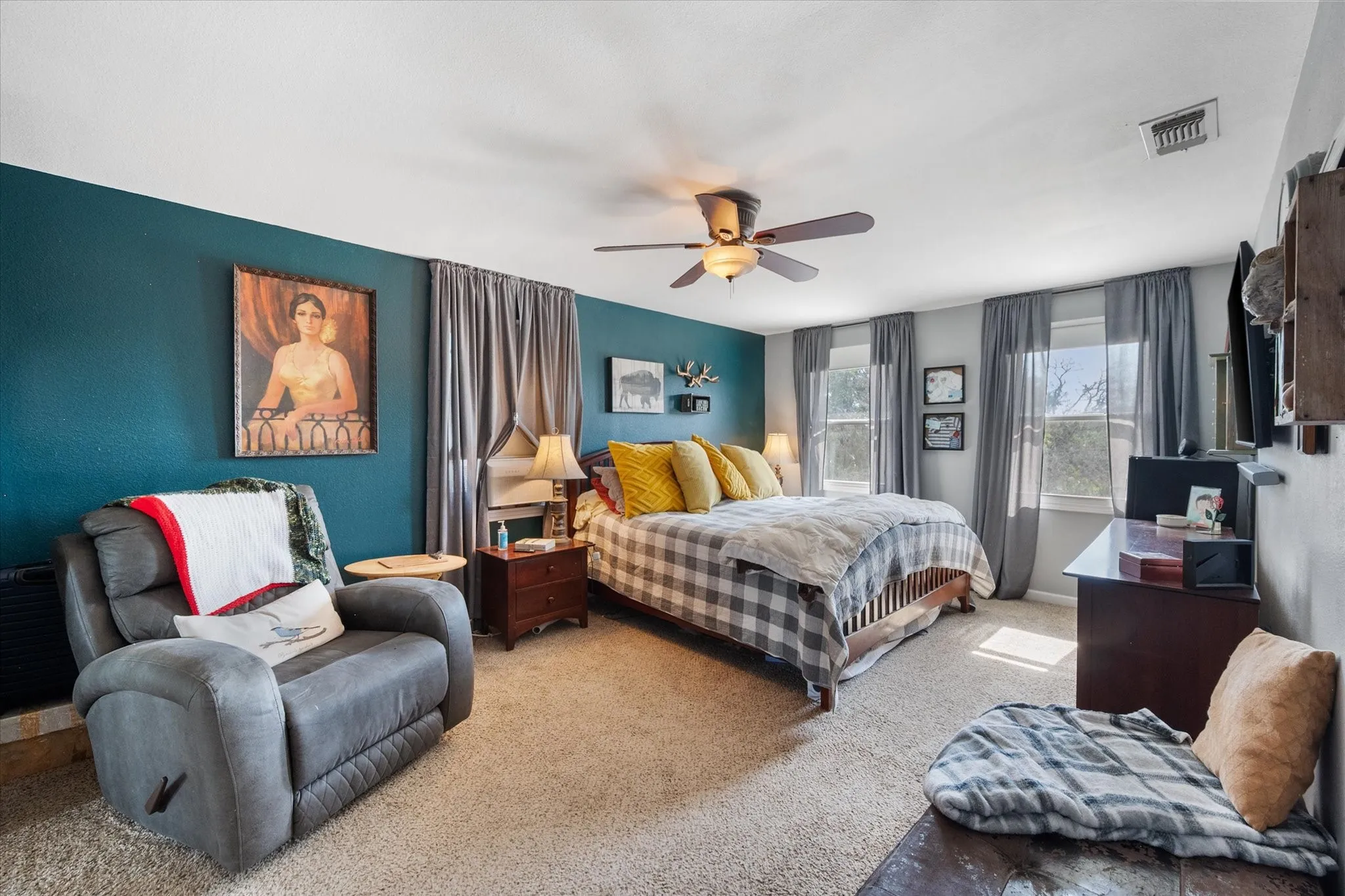 Carpeted bedroom featuring multiple windows with draperies, a ceiling fan with integrated lighting, and a prominent accent wall