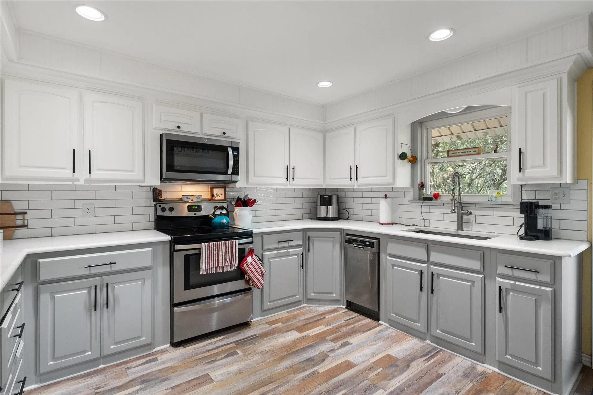 Contemporary kitchen featuring two-tone cabinetry, stainless steel appliances, a subway tile backsplash, recessed lighting, and wood-finish flooring