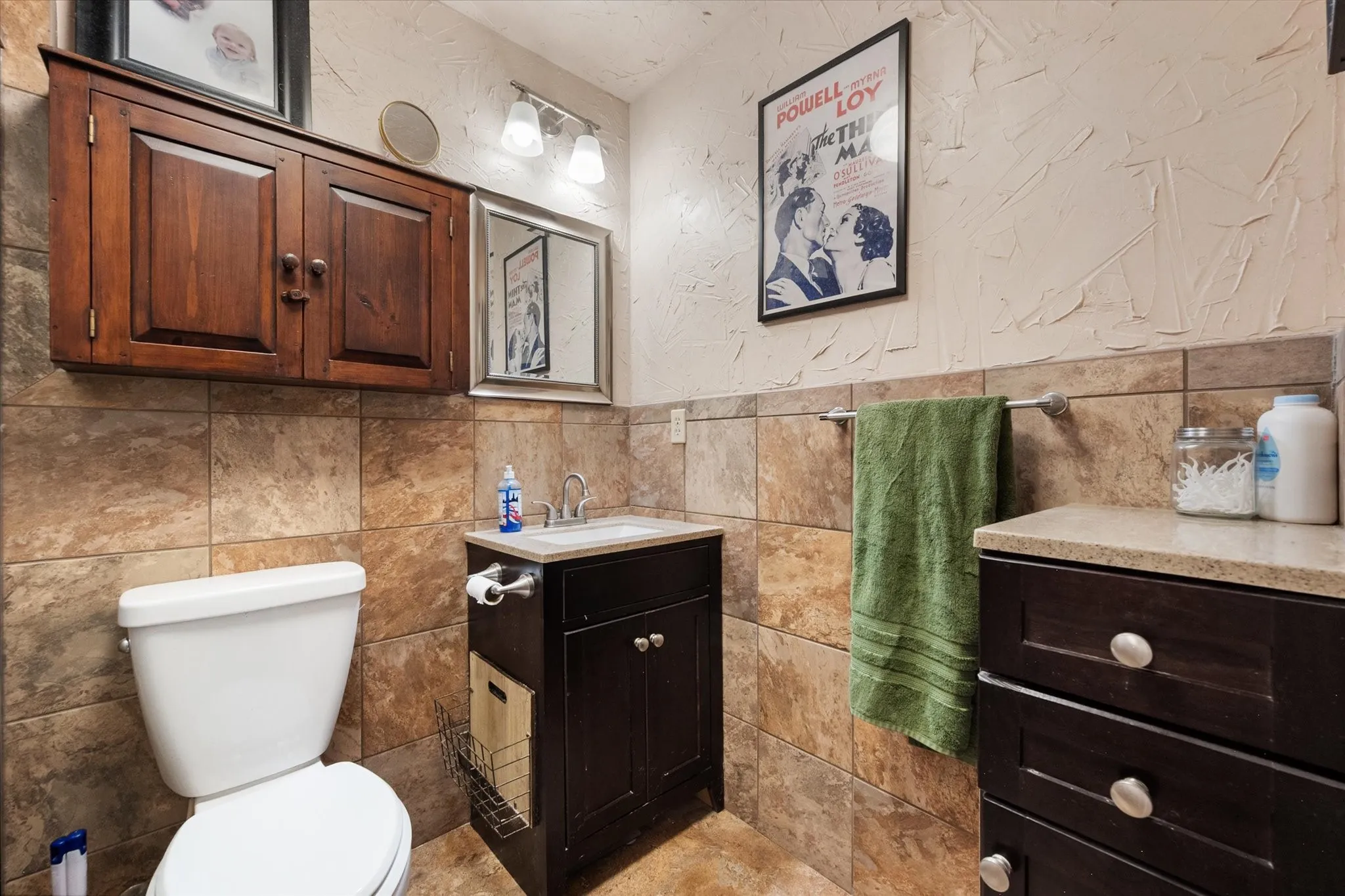 Tile wainscoting and flooring, a dark wood-finish vanity with countertop, and an additional dark wood-finish cabinet with drawers offer storage solutions