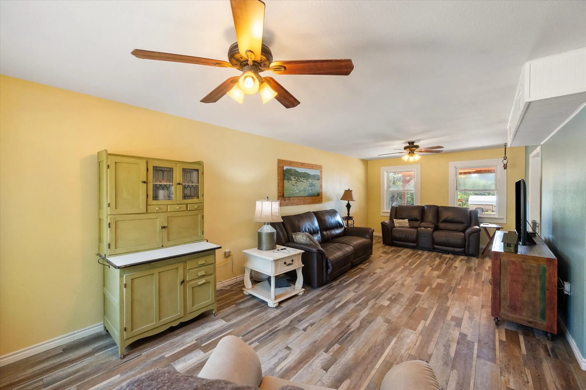 Spacious room featuring wood-finish flooring, light-colored walls, and multiple ceiling fans with integrated lighting