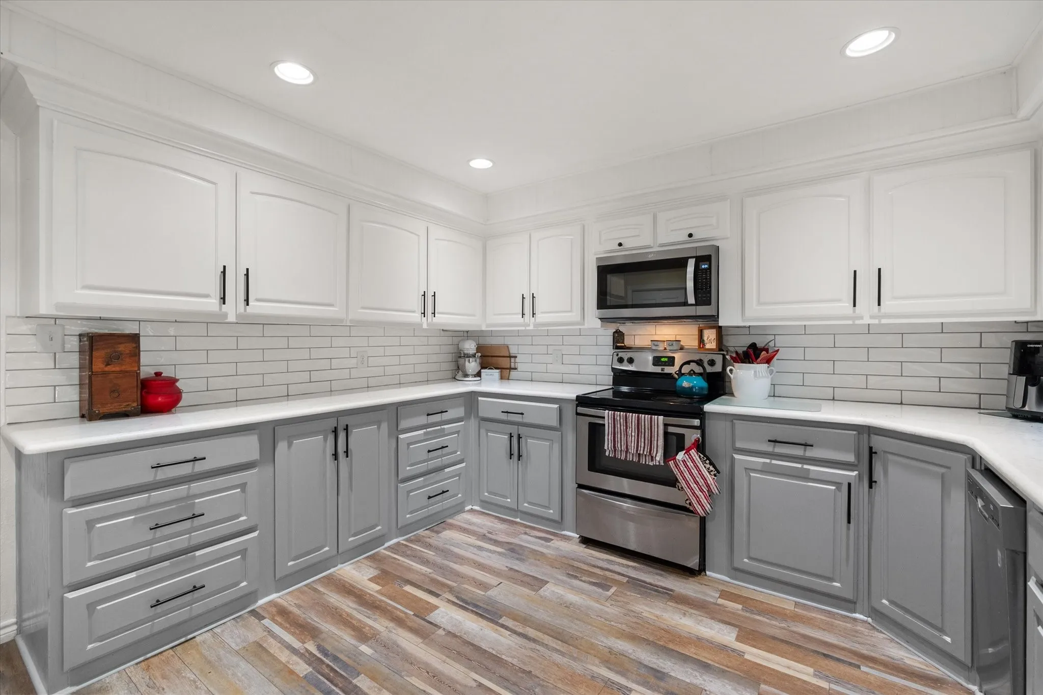 Kitchen featuring two-tone cabinetry, subway tile backsplash, stainless steel appliances, recessed lighting, and wood-finish flooring