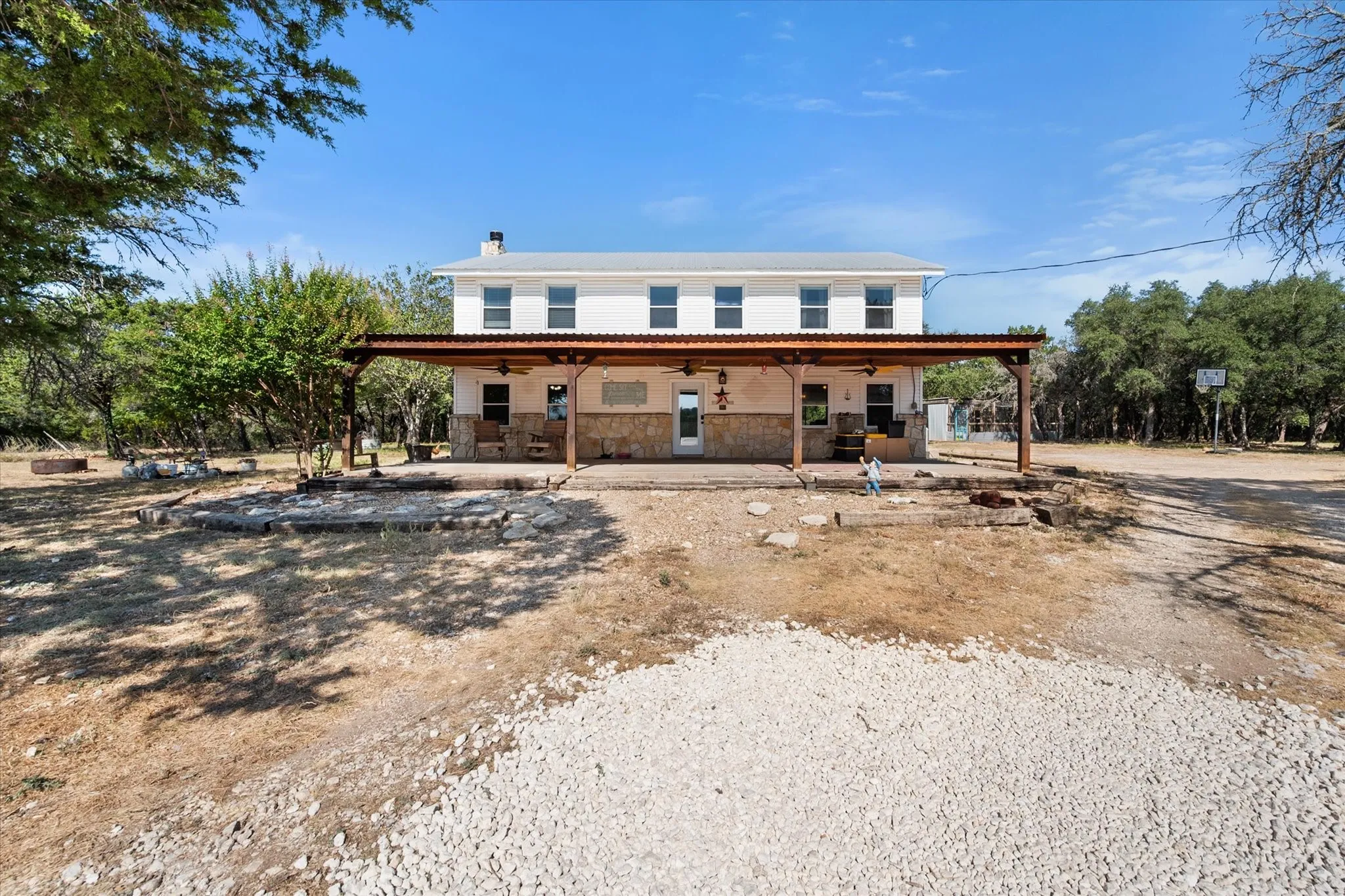 Two-story white exterior with stone accents, covered patio, multiple windows, and a gravel foreground