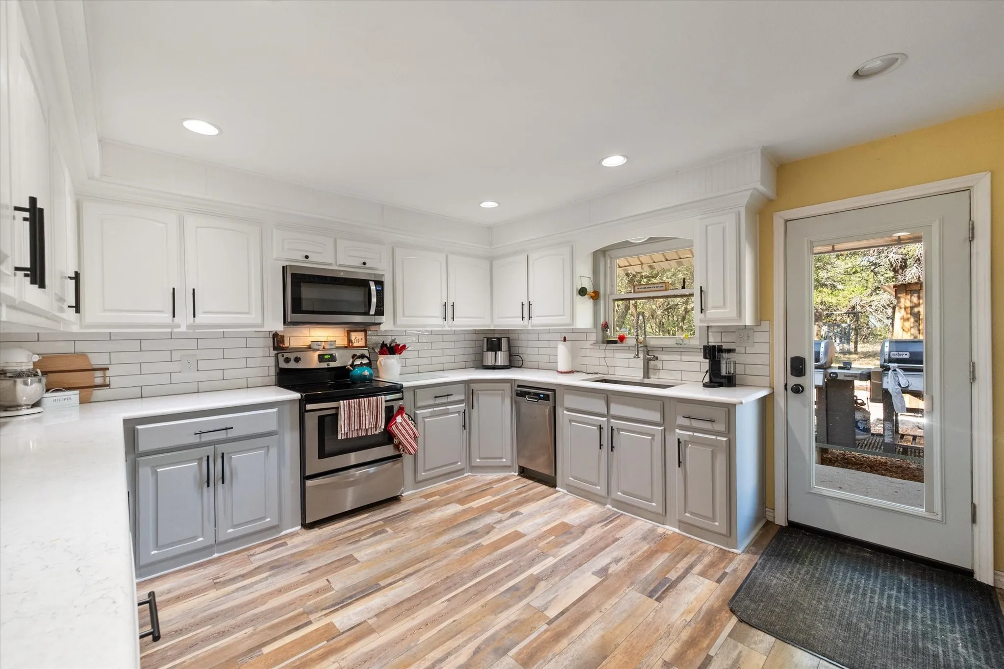 Kitchen featuring two-tone cabinetry, wood-finish flooring, stainless steel appliances, a subway tile backsplash, and recessed lighting