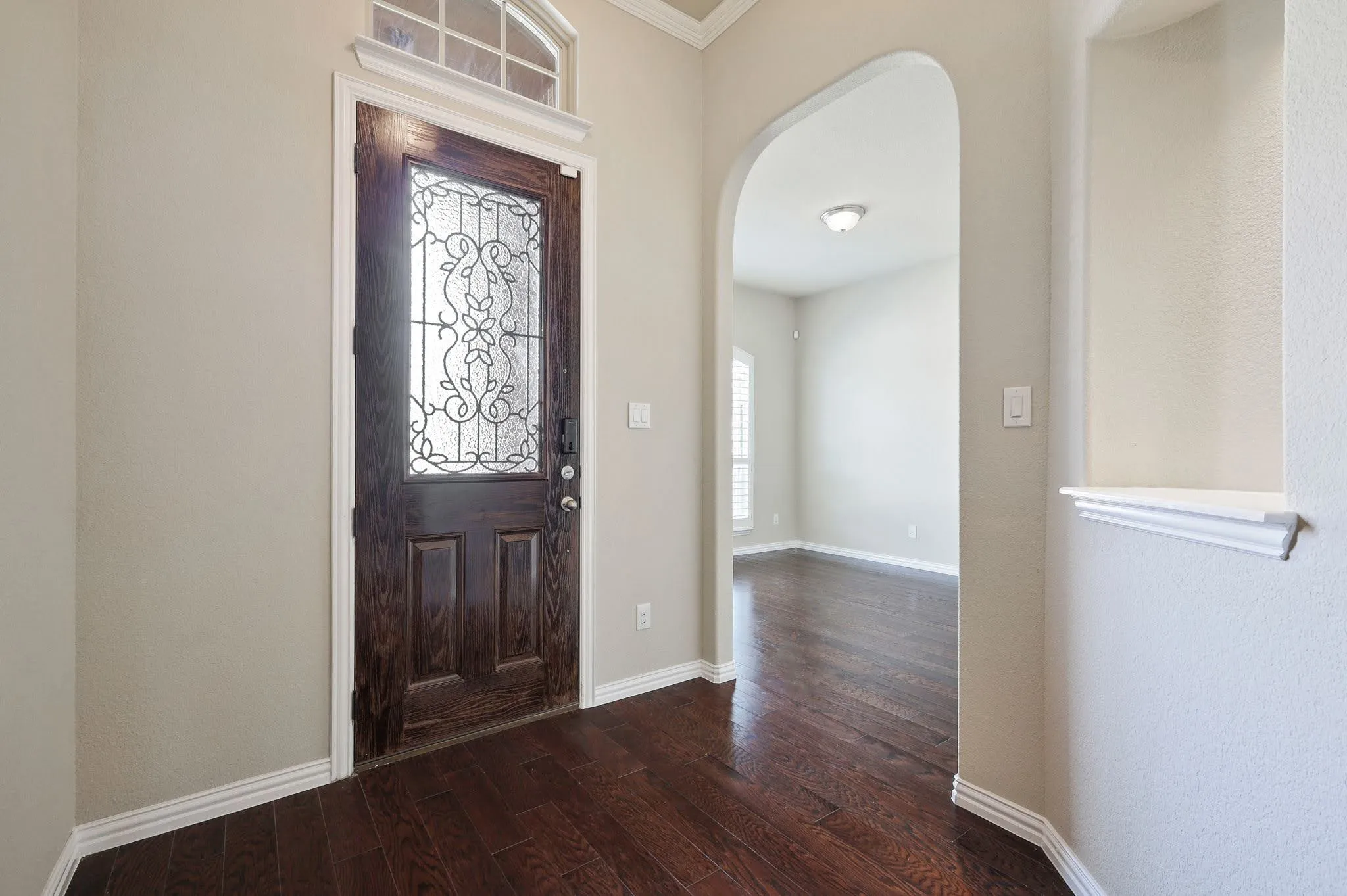 Dark wood-finish flooring, decorative glass entry door with transom window, arched entryway, and white trim molding