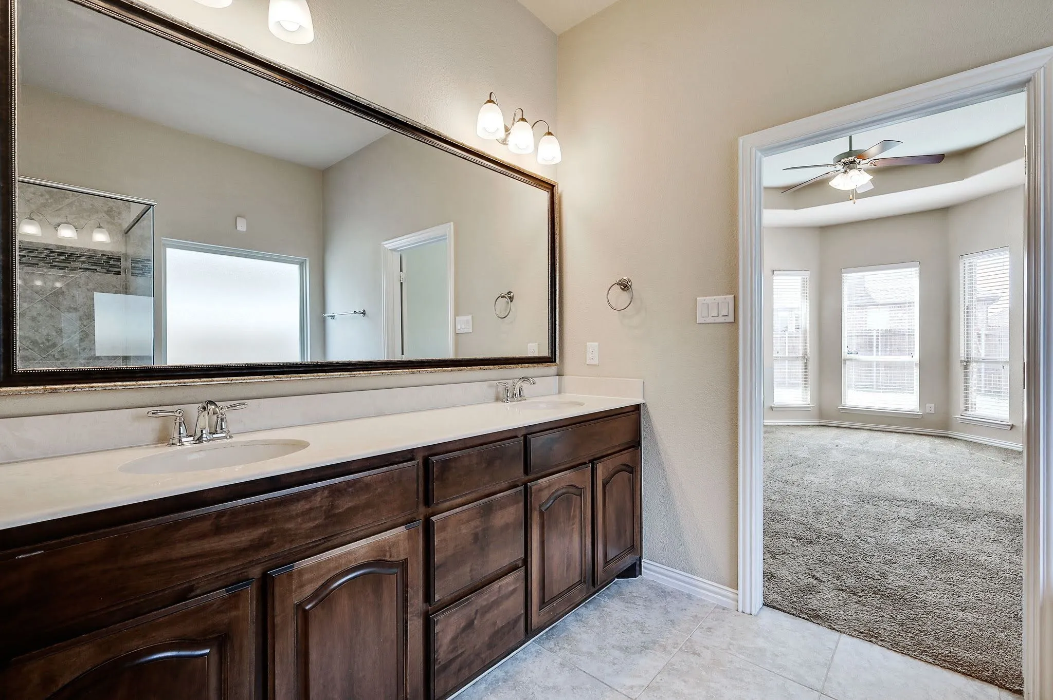 Double vanity with a light-toned countertop, wood-finish cabinetry, and a full-width mirror