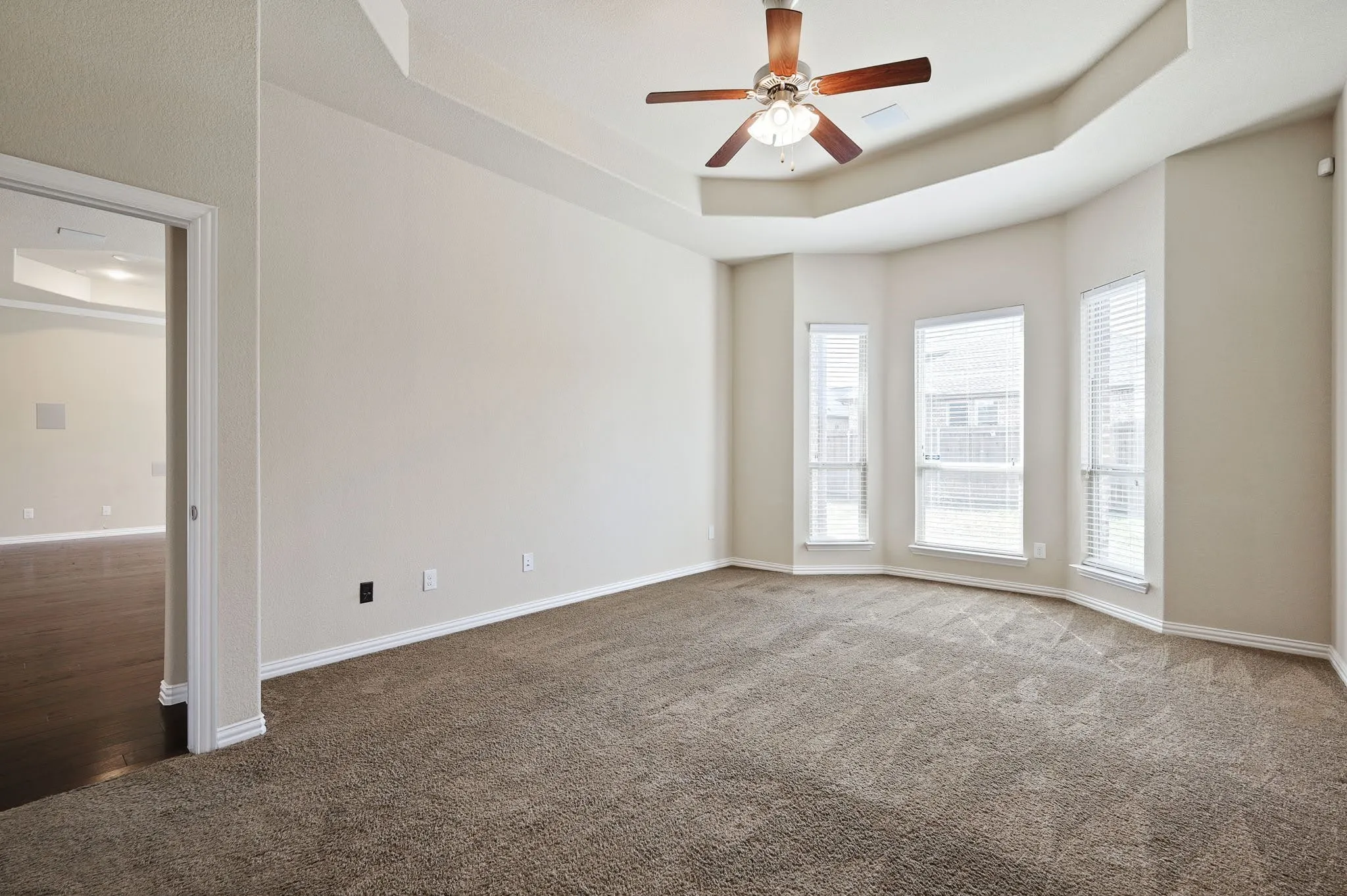 Tray ceiling with a ceiling fan, bay window with three vertical windows, and carpet flooring