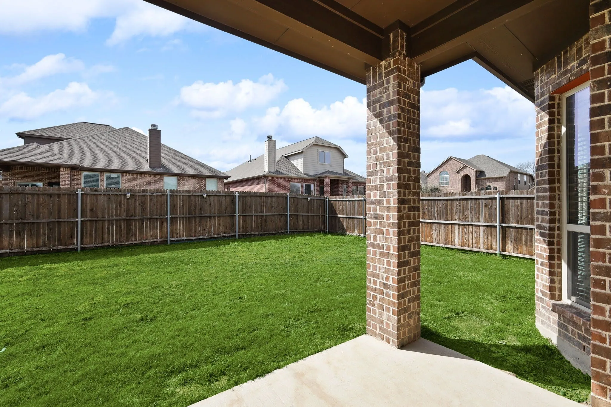 Covered patio with brick columns, concrete flooring, and a fully fenced backyard with a grass lawn