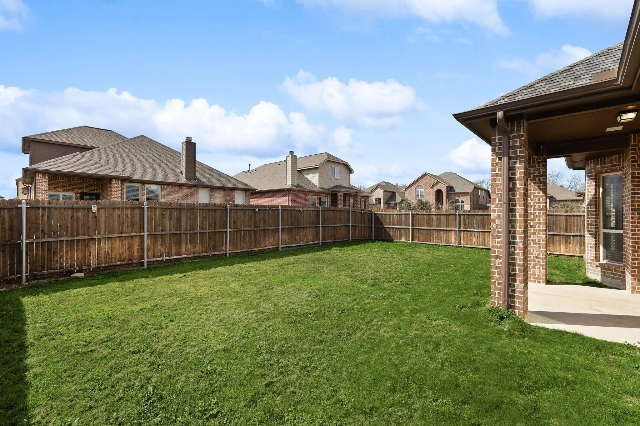 Spacious grassy yard, full perimeter privacy fencing, covered patio, brick exterior, and dark shingle roofing