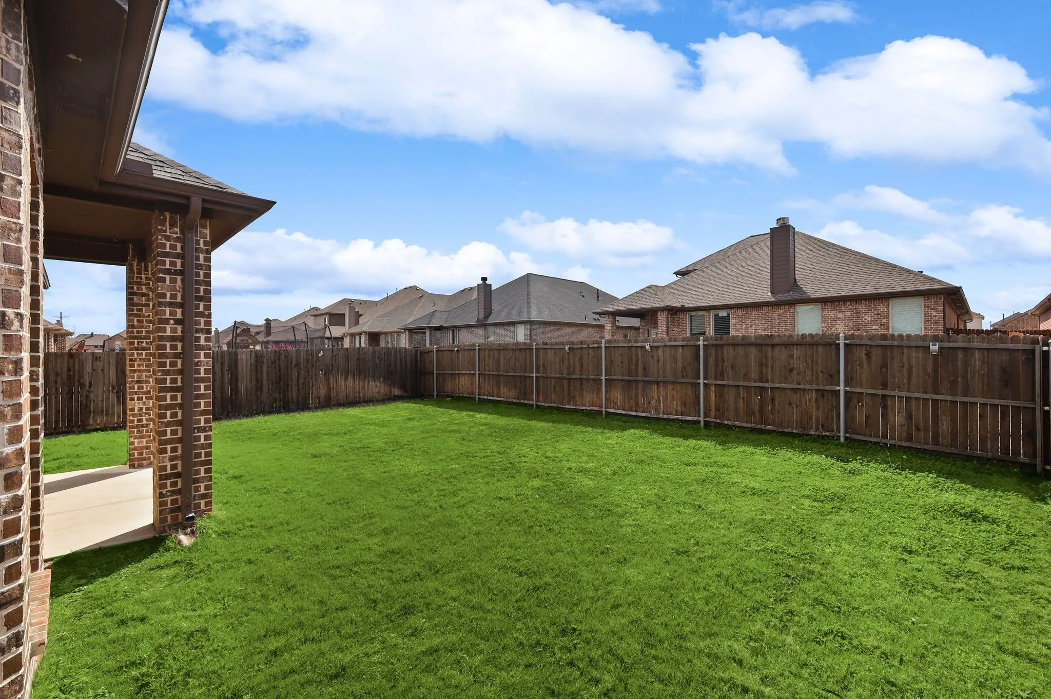 Expansive green lawn, wood privacy fence, covered patio, brick exterior, and a brown shingle roof