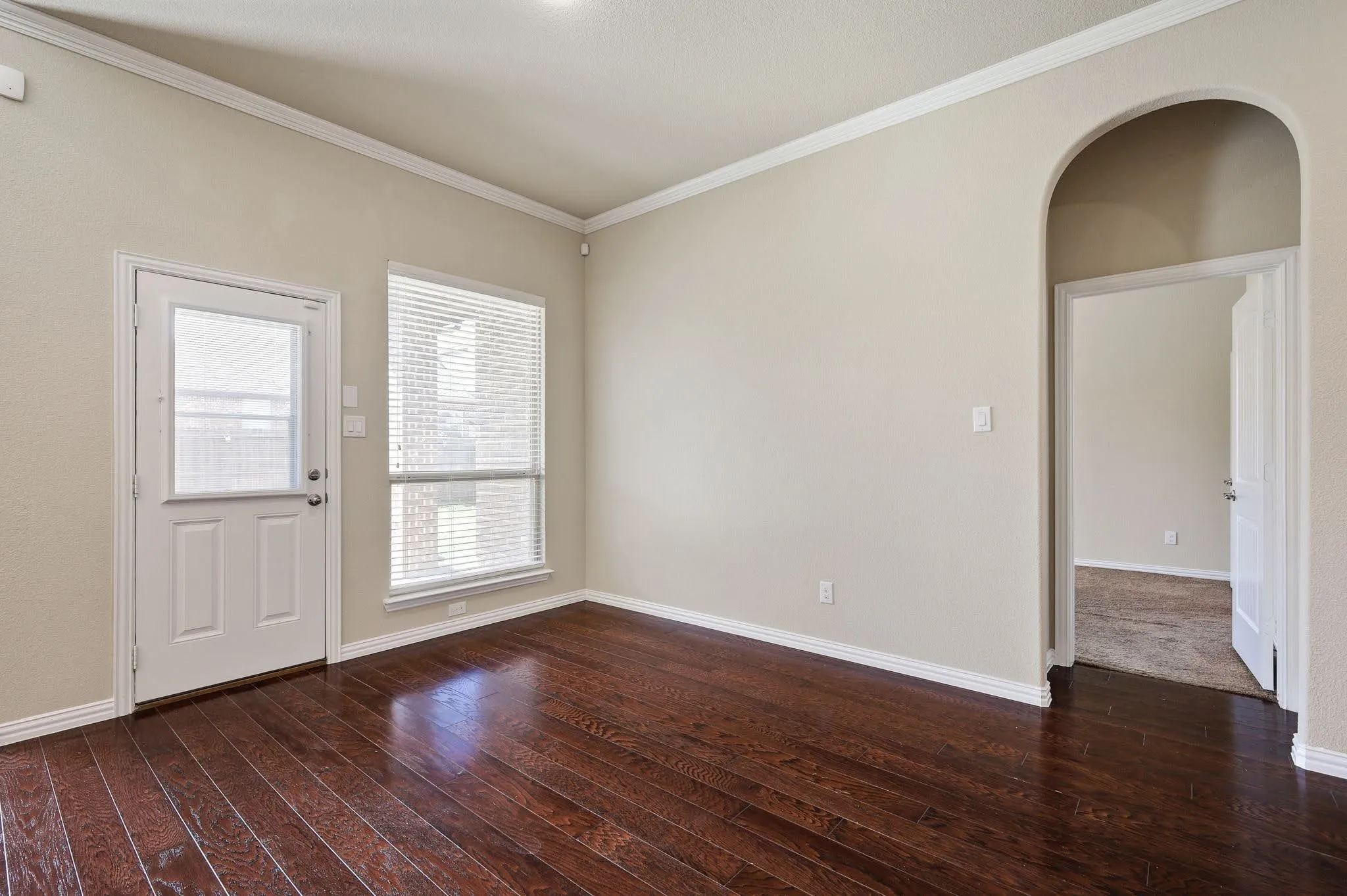 Dark wood-finish flooring, white crown molding, and a prominent arched entryway