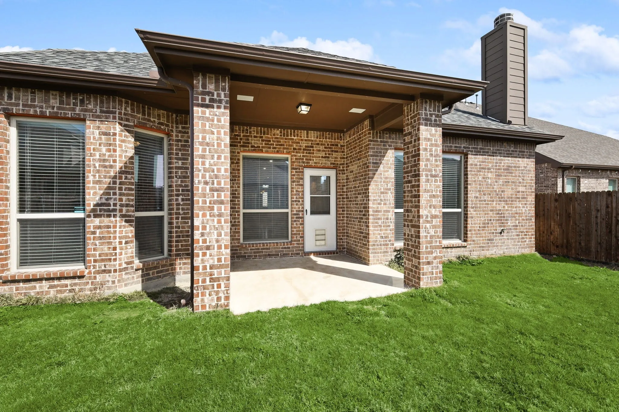 Covered patio with a concrete slab, brick exterior, and a fenced yard