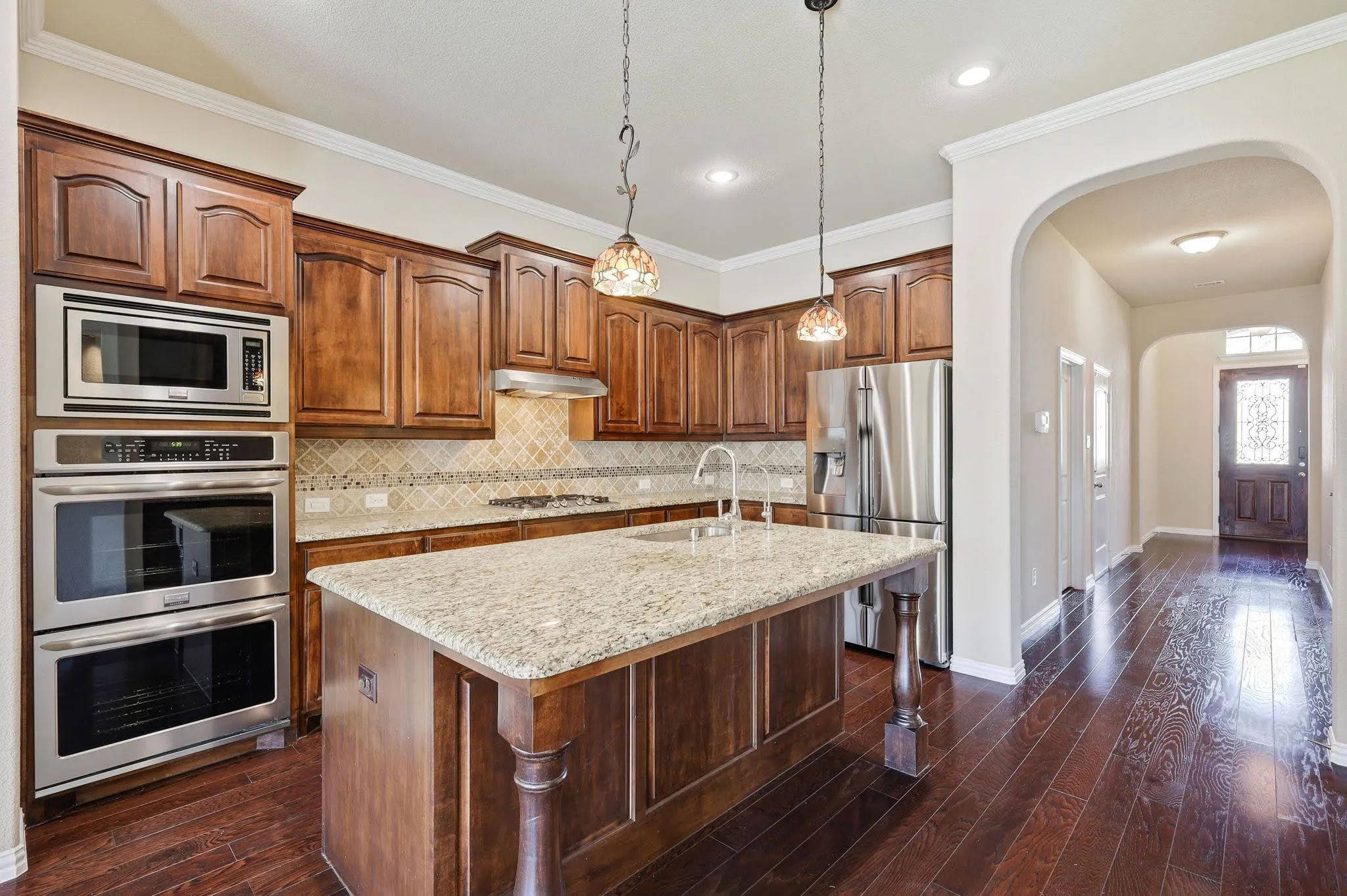 Kitchen featuring wood-finish flooring, a central island with a granite countertop, built-in stainless steel appliances, dark wood cabinetry, and a decorative tile backsplash