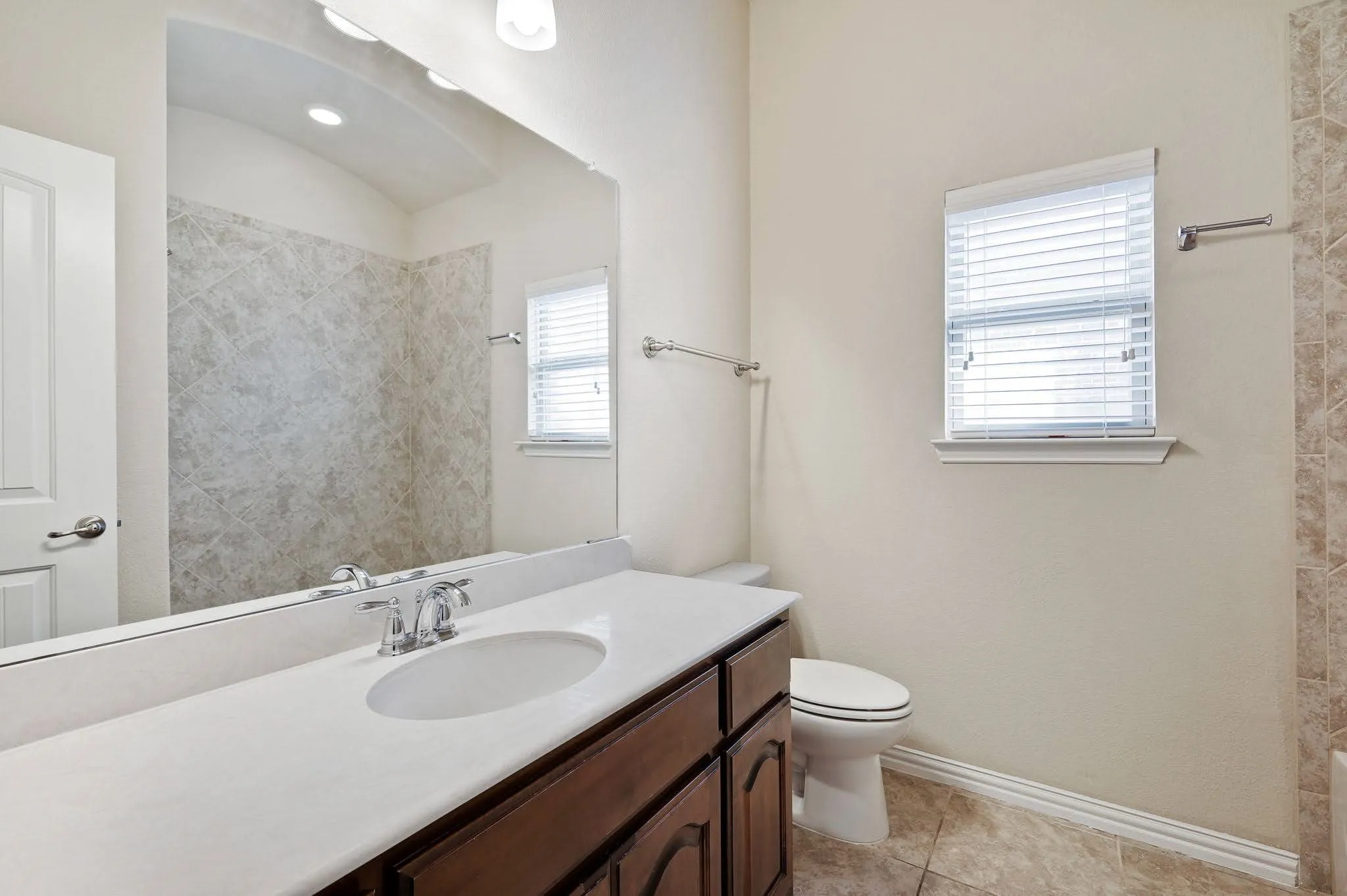 Wood-finish vanity with an integrated sink, polished chrome faucet, and expansive mirror