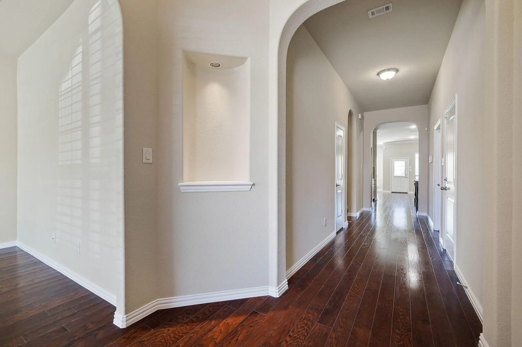 Arched doorways, recessed wall niche with accent lighting, wood-finish flooring, and bright white trim throughout