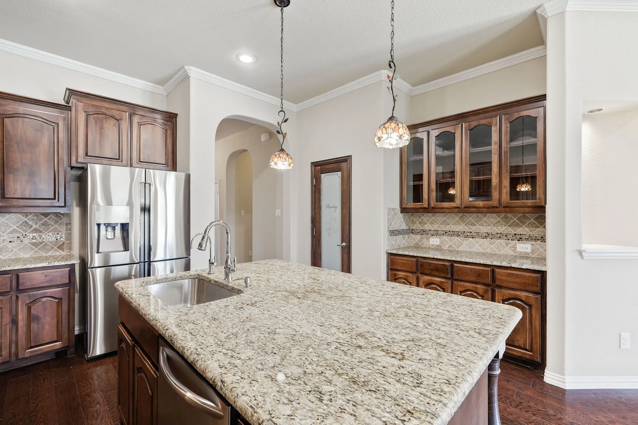 Spacious kitchen featuring a large island with an undermount sink, stainless steel appliances, dark wood cabinetry, and a tile backsplash