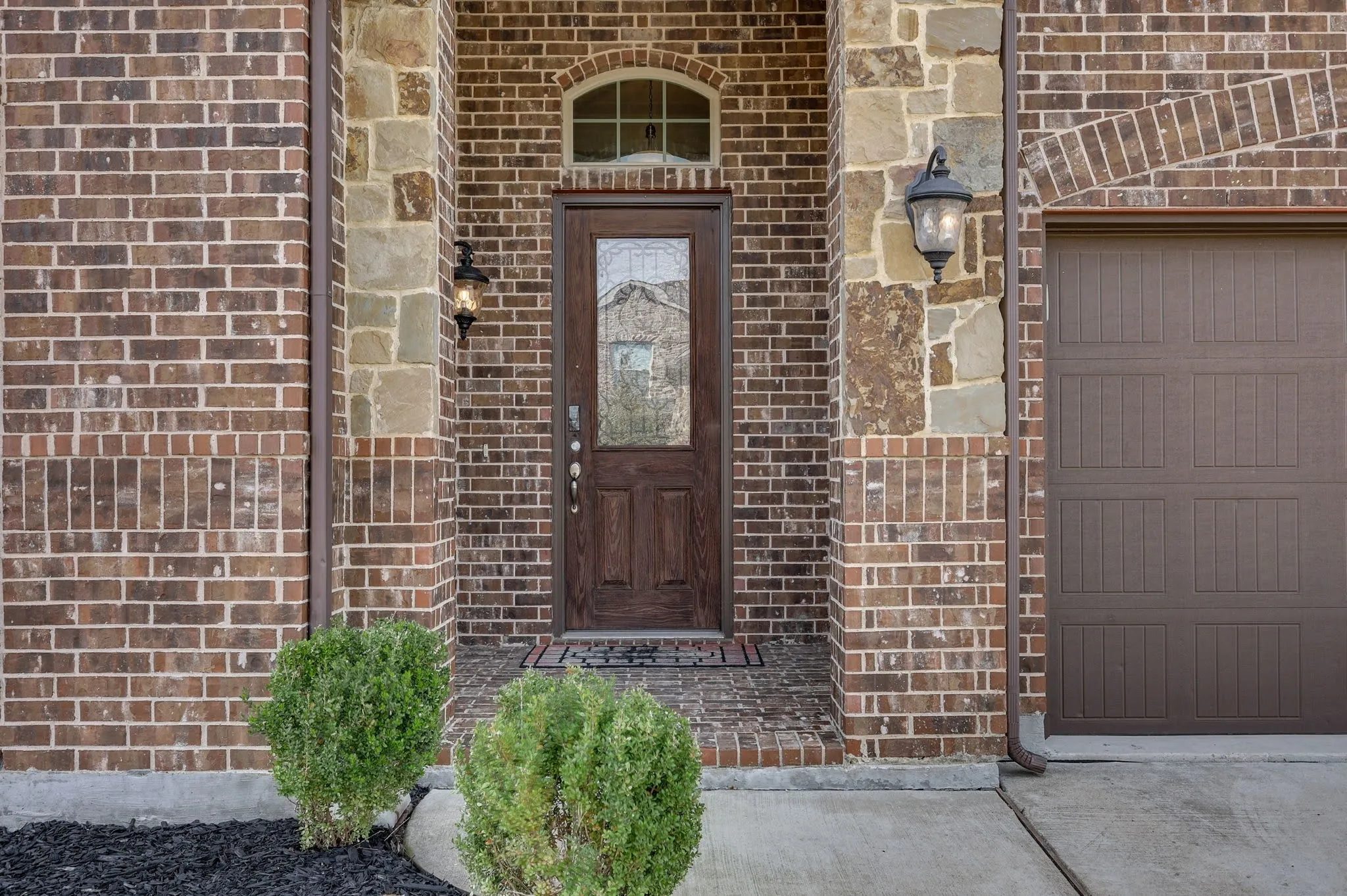 Brick and stone exterior with an arched entryway, decorative front door with leaded glass, and a paneled garage door
