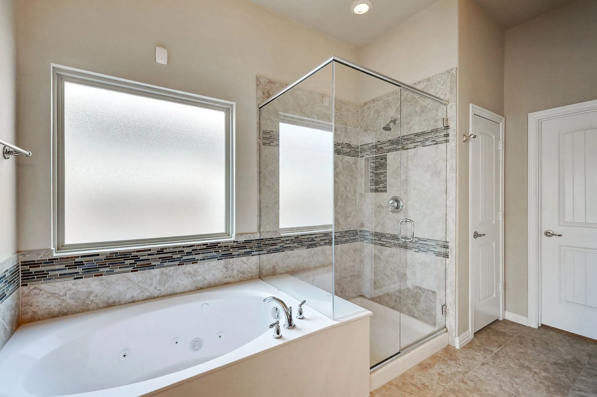 Built-in jetted tub with polished chrome fixtures, glass-enclosed shower with tile surround, mosaic tile accents, and frosted privacy window