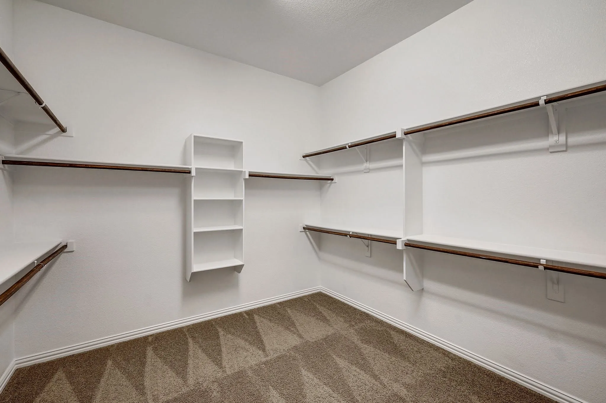 Walk-in closet featuring white built-in shelving, wood-finish hanging rods, and patterned carpeting