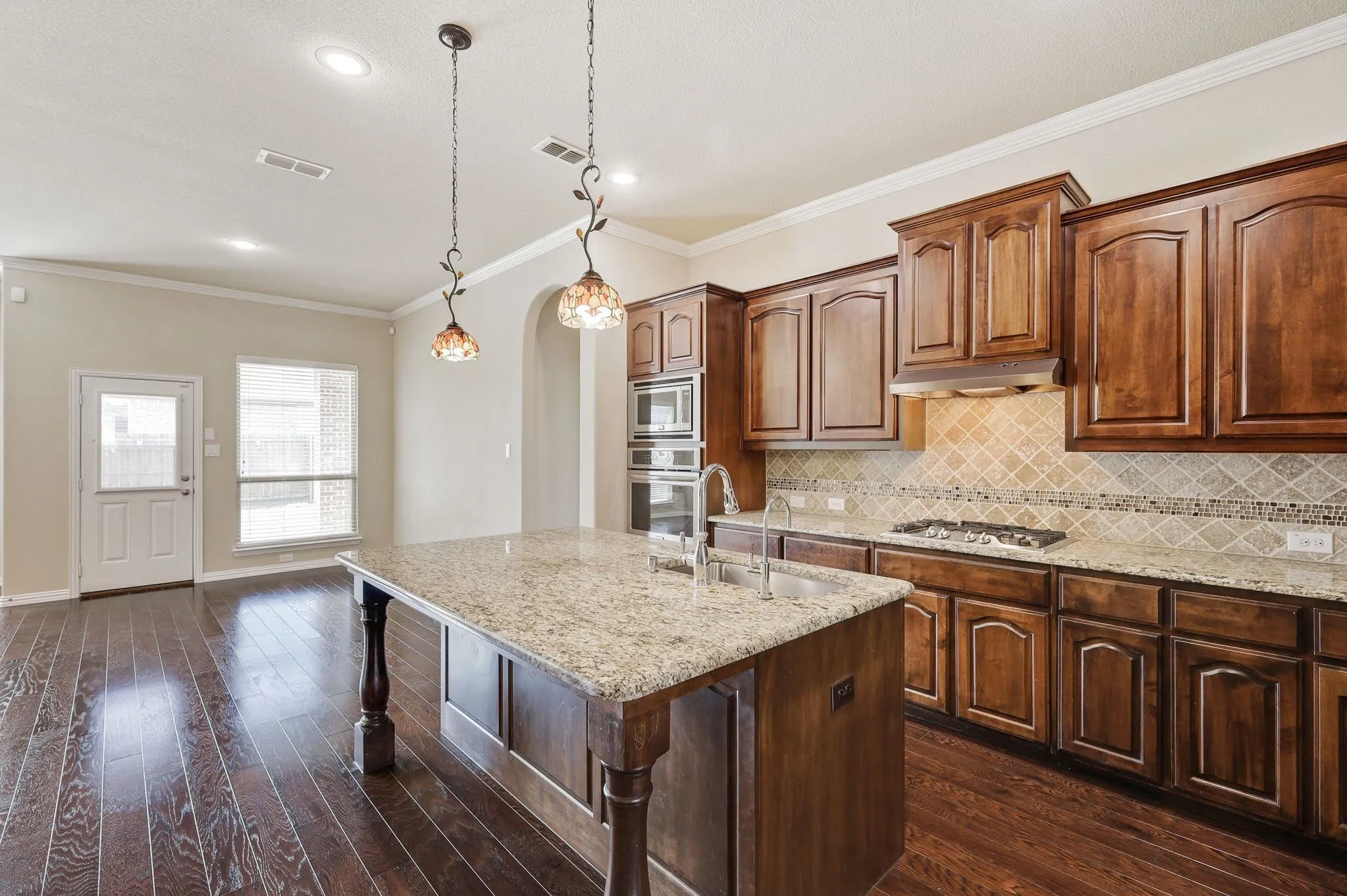 Kitchen featuring wood-finish flooring, a large island with a stone countertop, built-in stainless steel appliances, a gas cooktop, and custom cabinetry with decorative hardware