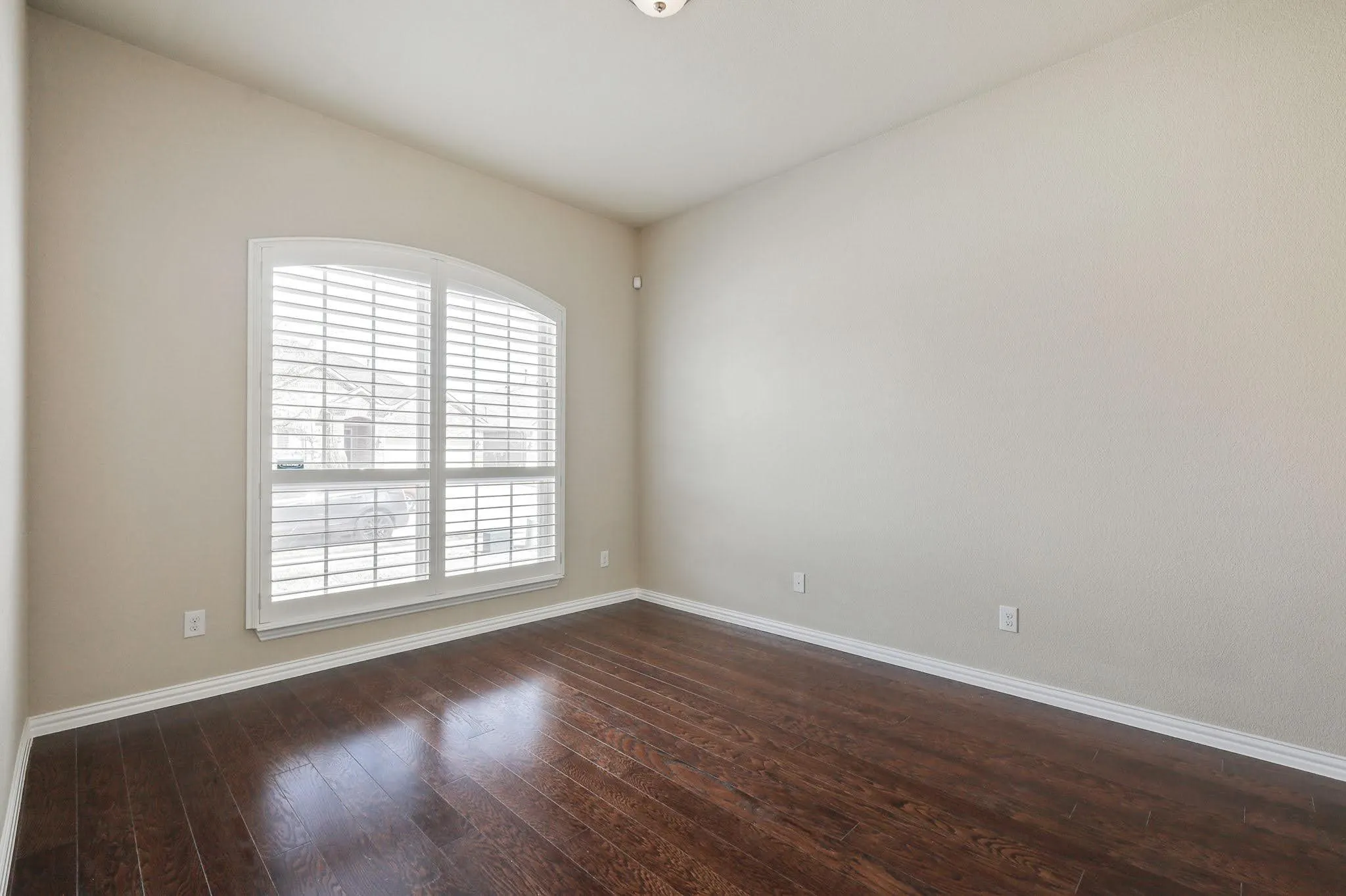 Arched window with plantation shutters, wood-finish flooring, neutral wall tones, and white trim