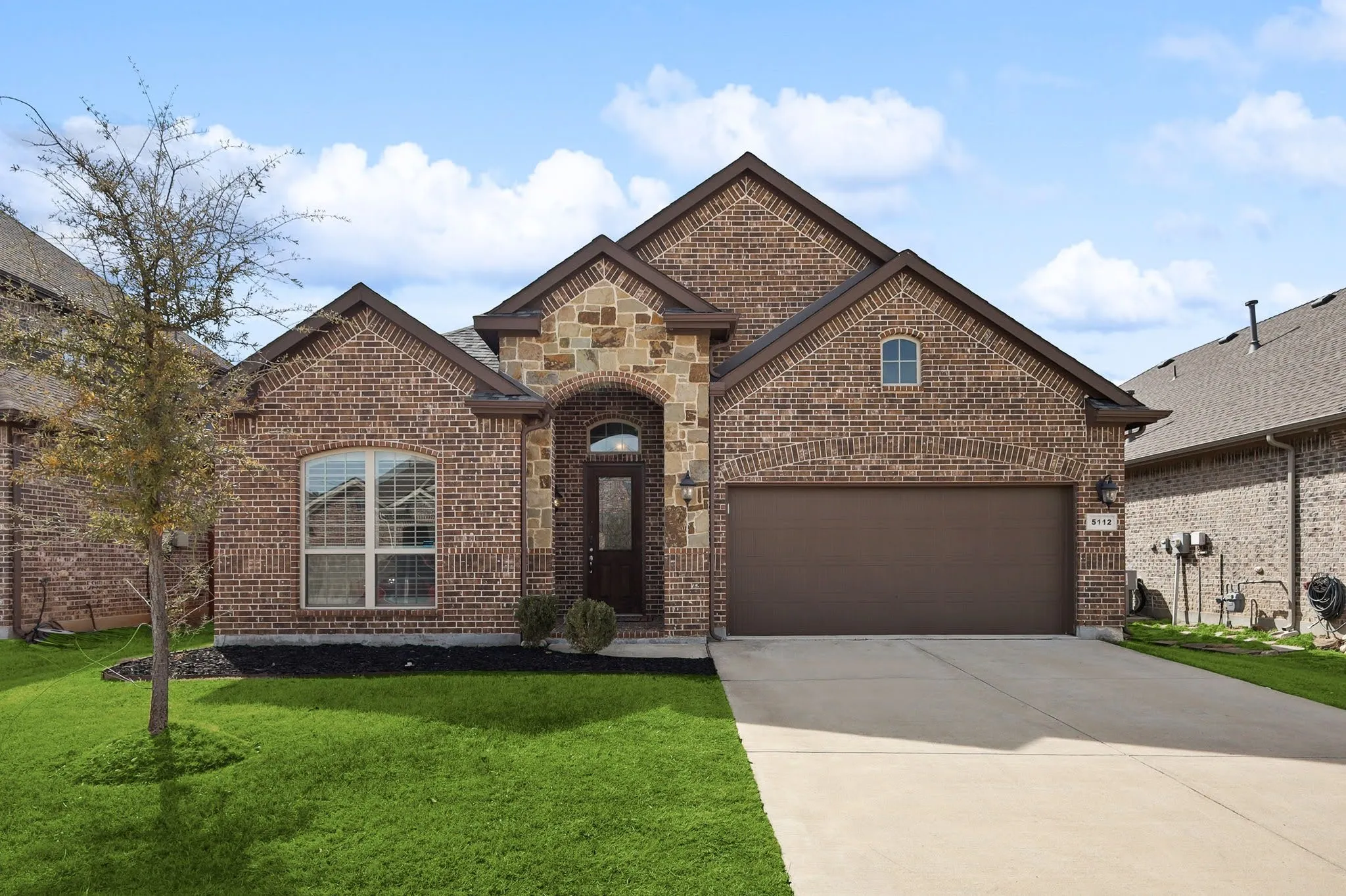 Brick exterior with stone accents, arched entry, attached two-car garage, concrete driveway, and a front yard with landscaping