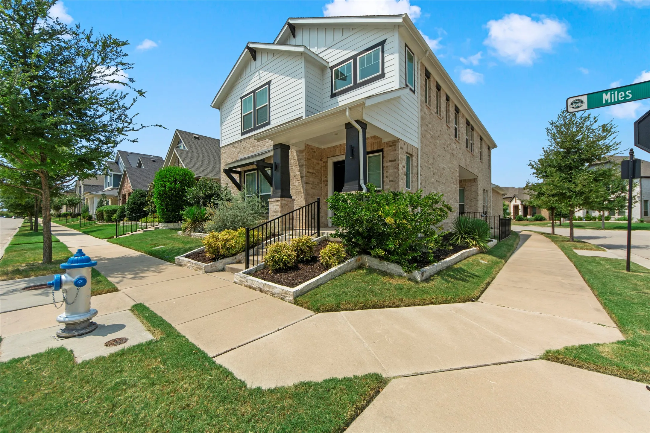 Charming two-story home featuring a brick and fiber cement exterior, welcoming front porch with railings, and a professionally landscaped front yard with mature trees, manicured lawn, and ornamental plantings