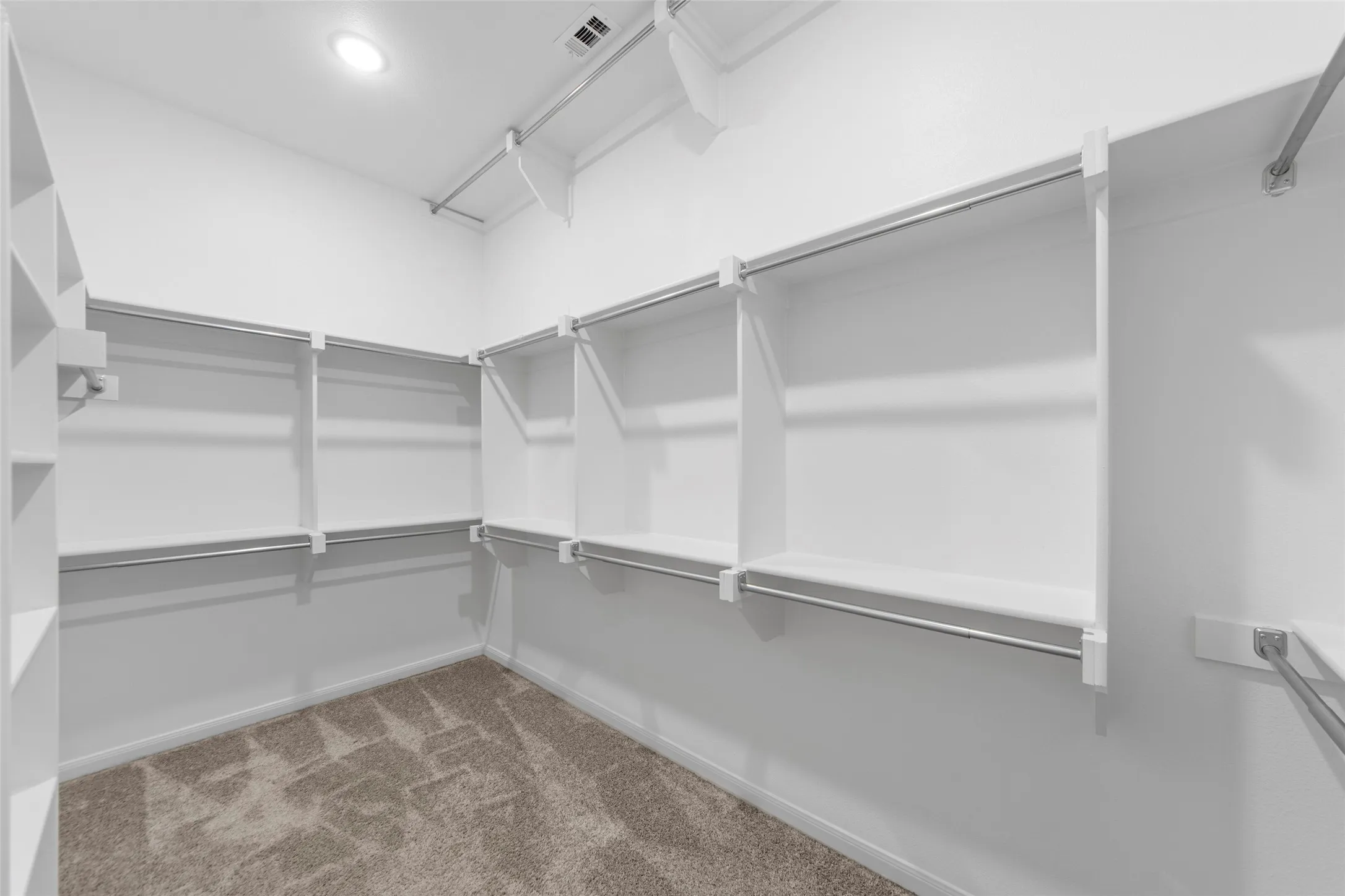 Spacious walk-in closet featuring custom shelving and hanging rods throughout, soft recessed lighting, and plush carpeted flooring