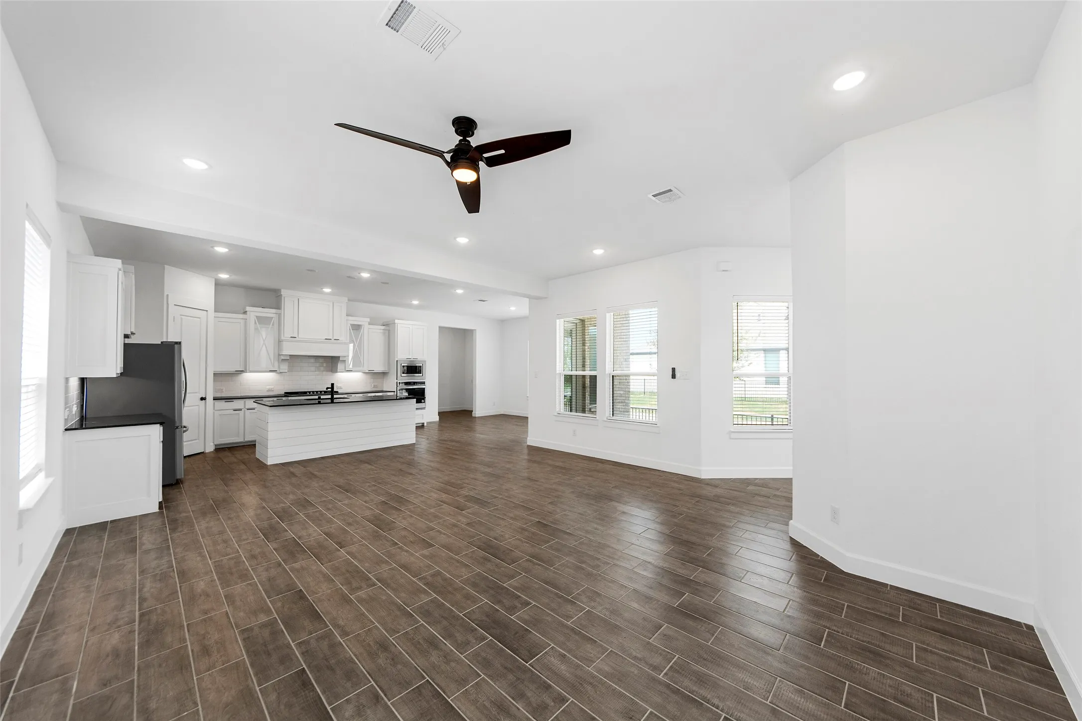 Open-concept living area featuring wood-finish tile flooring, recessed lighting, and a contemporary ceiling fan