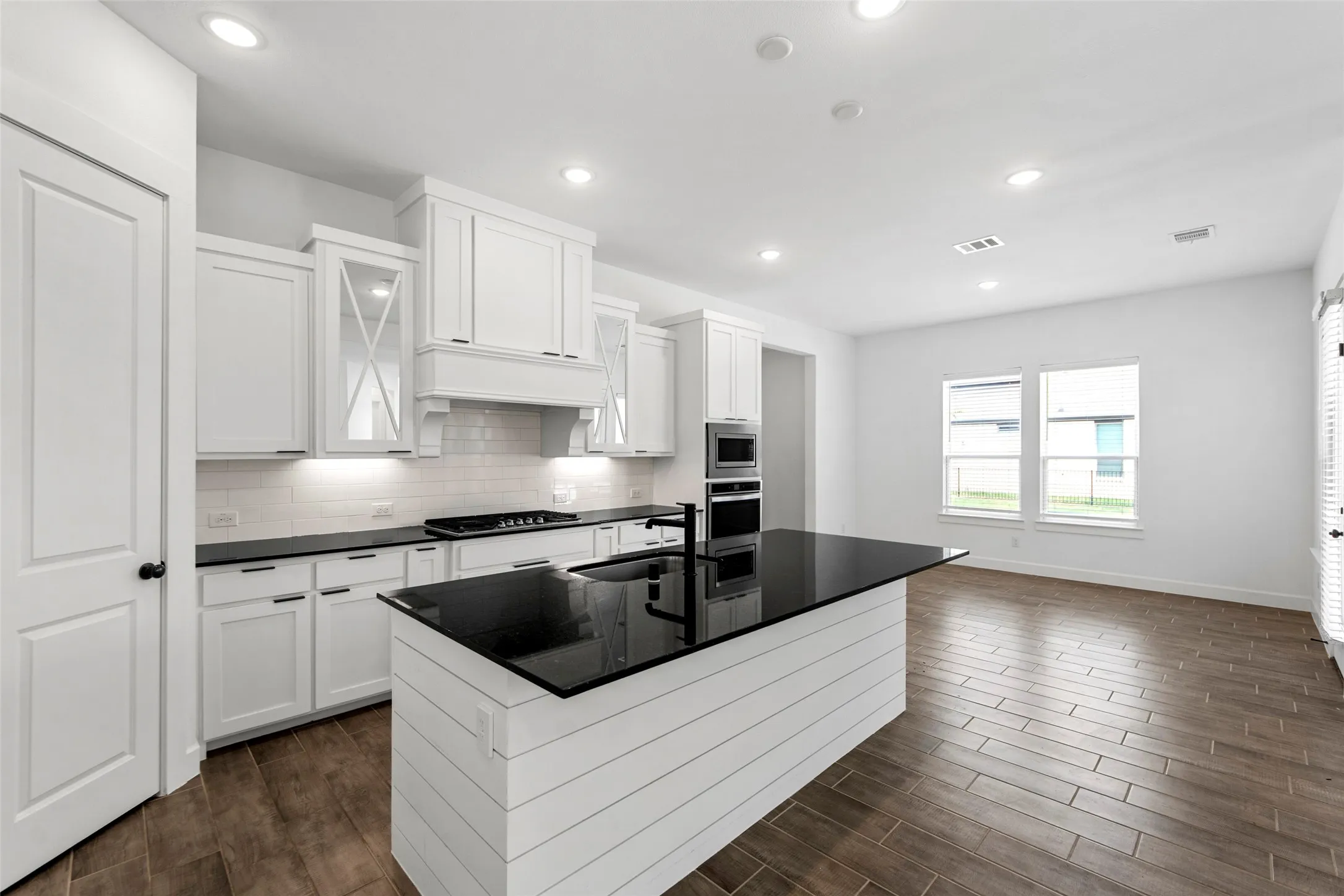 Bright kitchen featuring white cabinetry, dark countertops, a central island with shiplap detail, stainless steel appliances, and wood-finish flooring