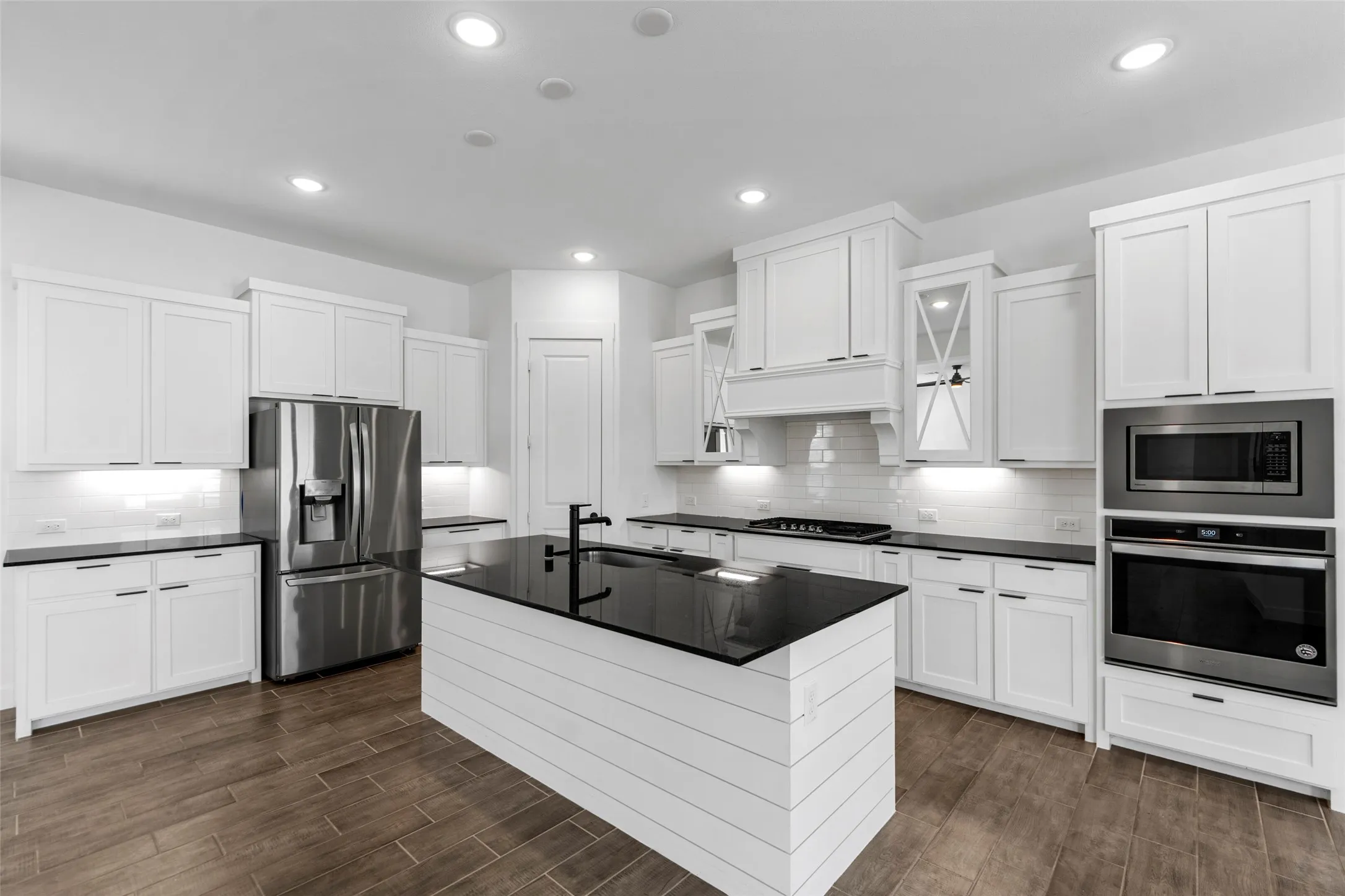 Kitchen featuring white shaker cabinetry, black countertops, wood-finish flooring, stainless steel appliances, and an expansive island