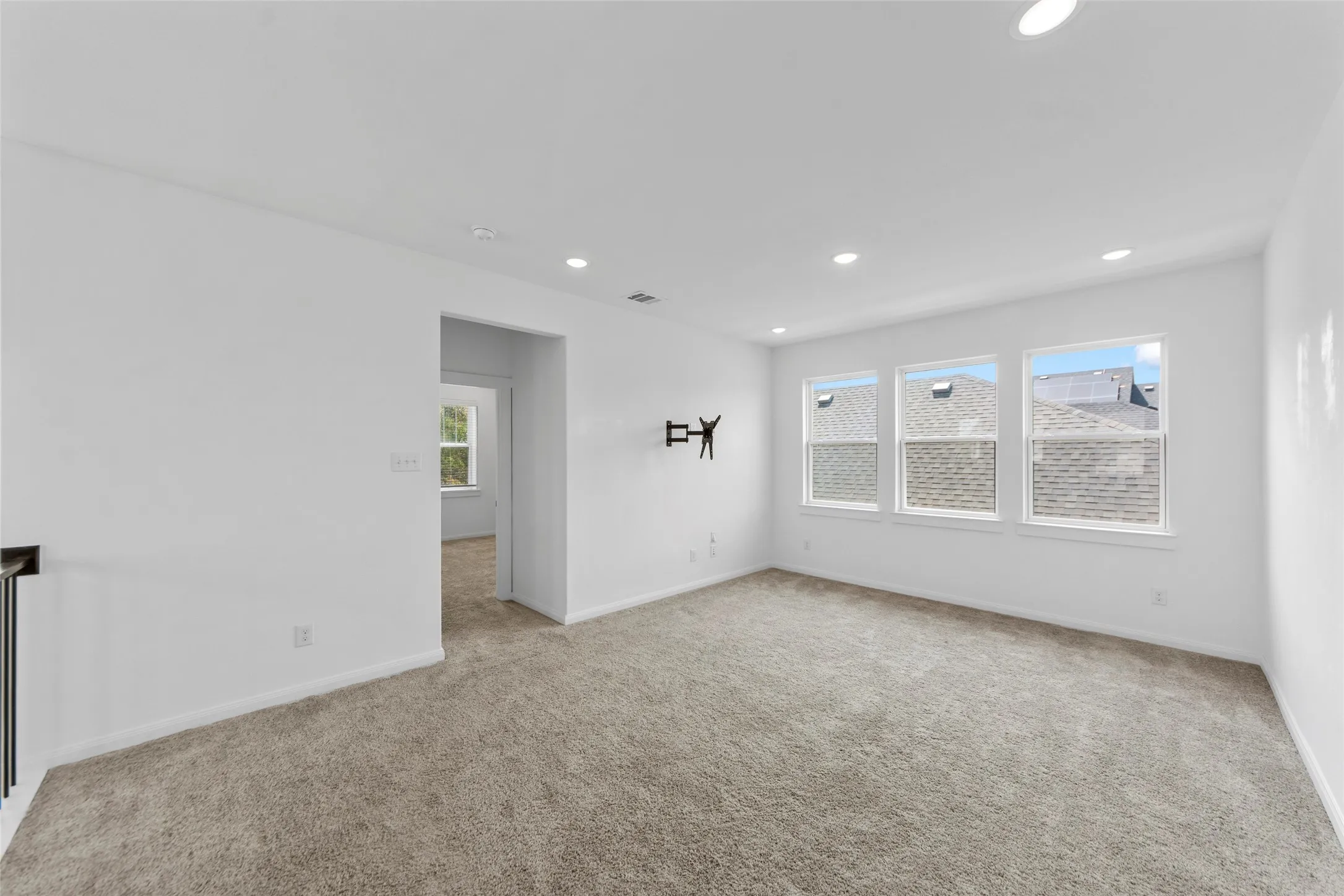 Bright secondary bedroom featuring recessed ceiling lighting, expansive windows with natural light, neutral carpet flooring, and seamless access to adjacent spaces through a wide doorway