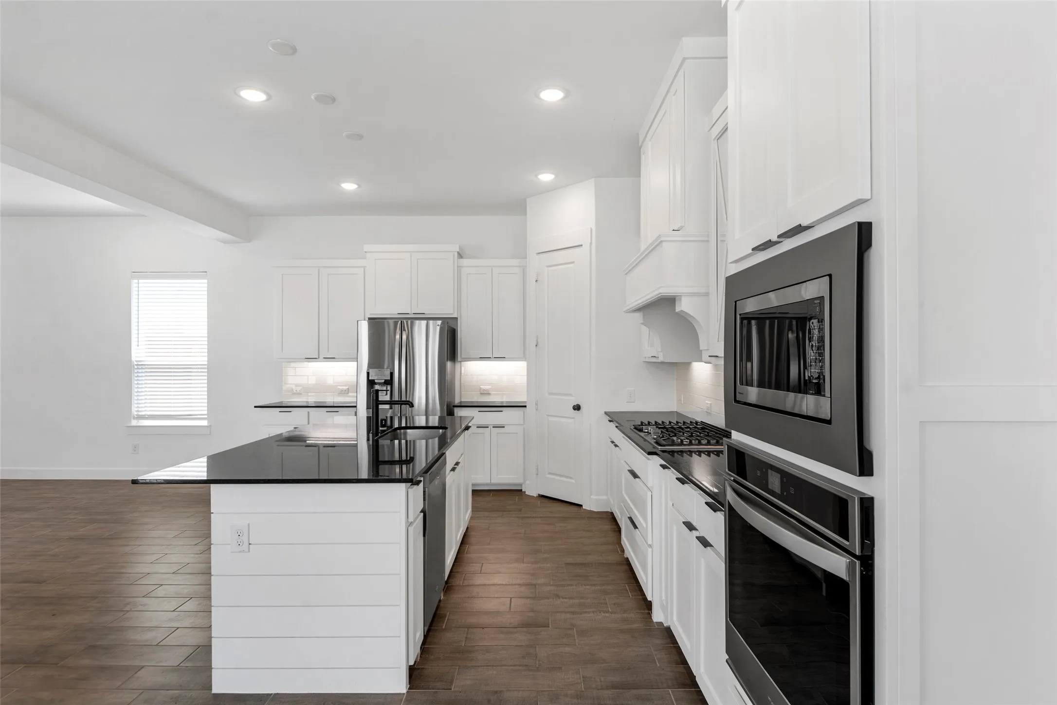 Contemporary kitchen featuring white cabinetry, dark countertops, a large island with a sink, stainless steel appliances, and wood-finish flooring
