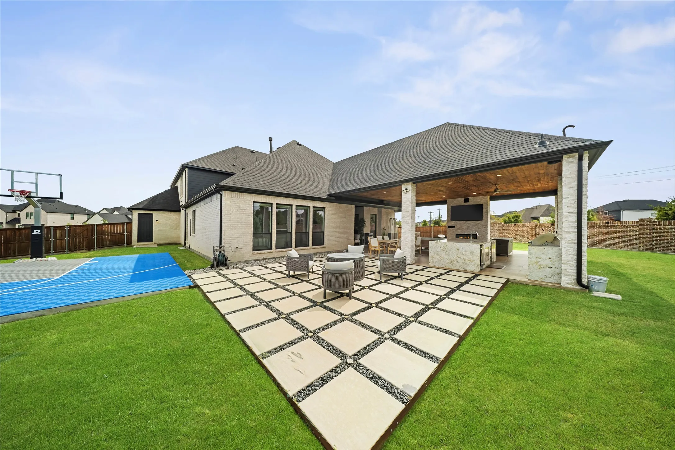 Expansive outdoor entertaining area featuring a covered patio with a built-in outdoor kitchen, stone-clad columns, a decorative wood ceiling, and a paver patio with a gravel inlay