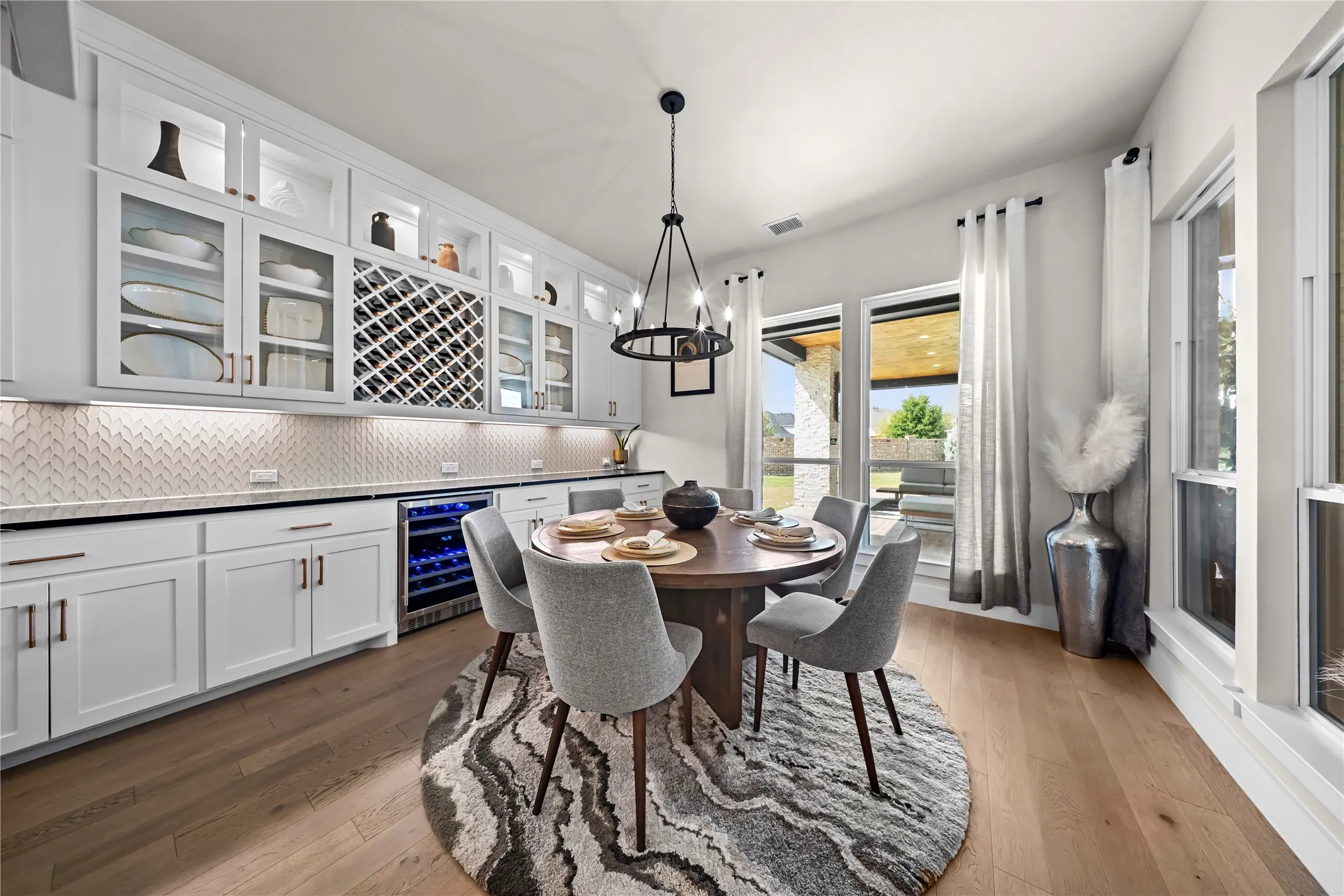 Built-in cabinetry with glass-front uppers, herringbone-patterned backsplash, wood-finish flooring, integrated wine refrigerator, and multiple large windows