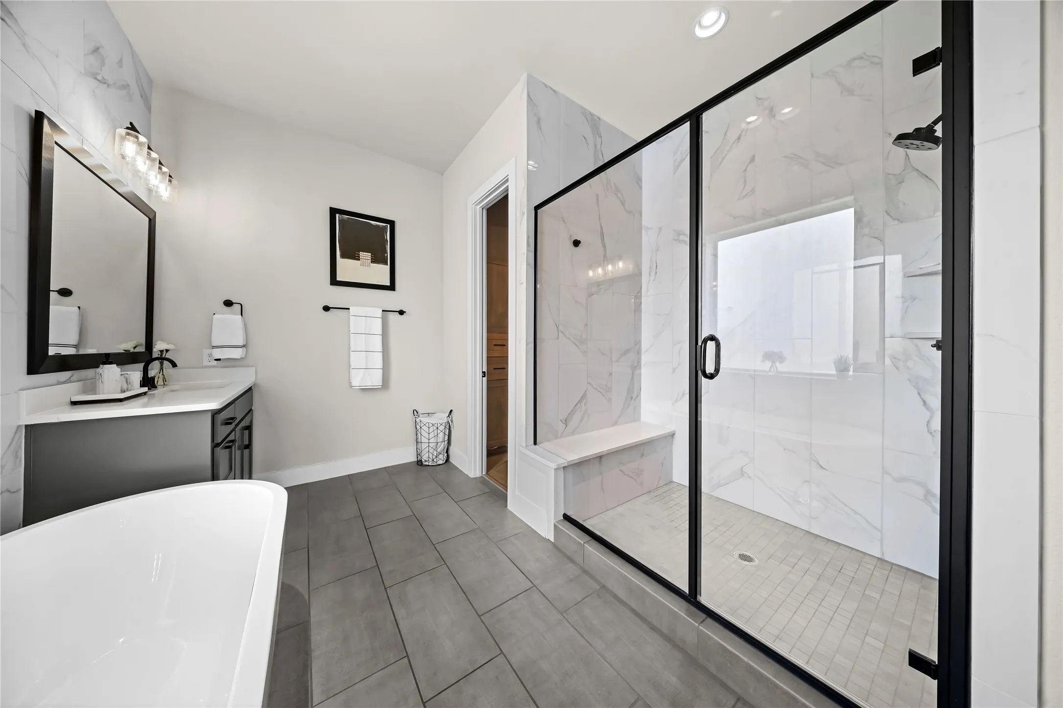 Freestanding soaking tub, walk-in shower with tiled walls and glass enclosure, gray floor tile, and single vanity with solid surface countertop