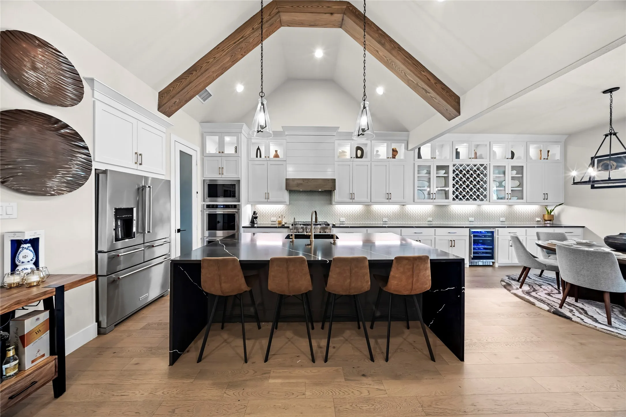 Vaulted ceiling with exposed wood beams, large kitchen island with waterfall counter, built-in wine storage, stainless steel appliances, and wood-finish flooring