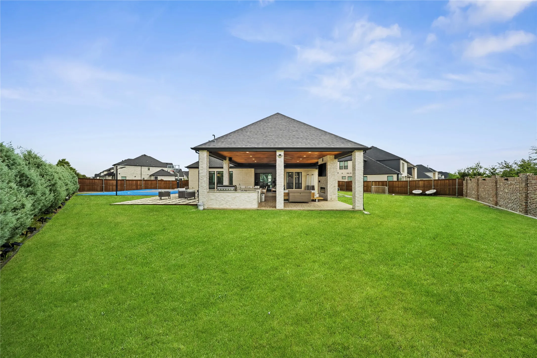 Expansive green lawn, covered patio with recessed lighting, integrated outdoor kitchen, and a sport court