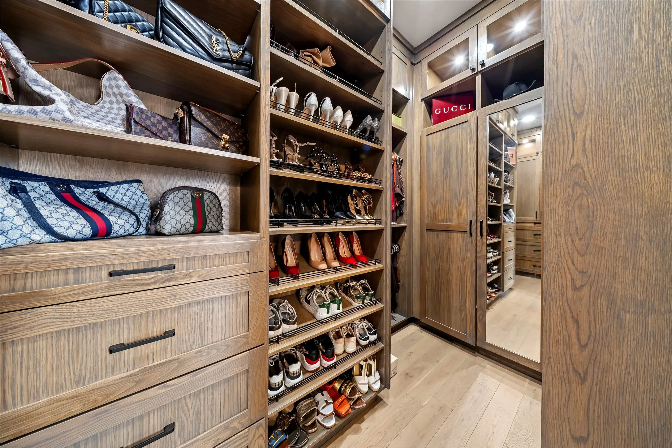 Custom closet system featuring wood-finish cabinetry, integrated shelving, pull-out drawers, and recessed lighting