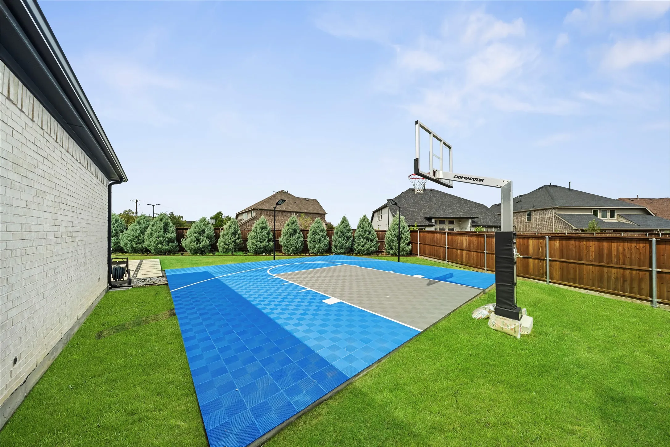 Expansive backyard featuring a full basketball court with blue and gray surfacing, a built-in basketball hoop, and a perimeter of manicured lawn