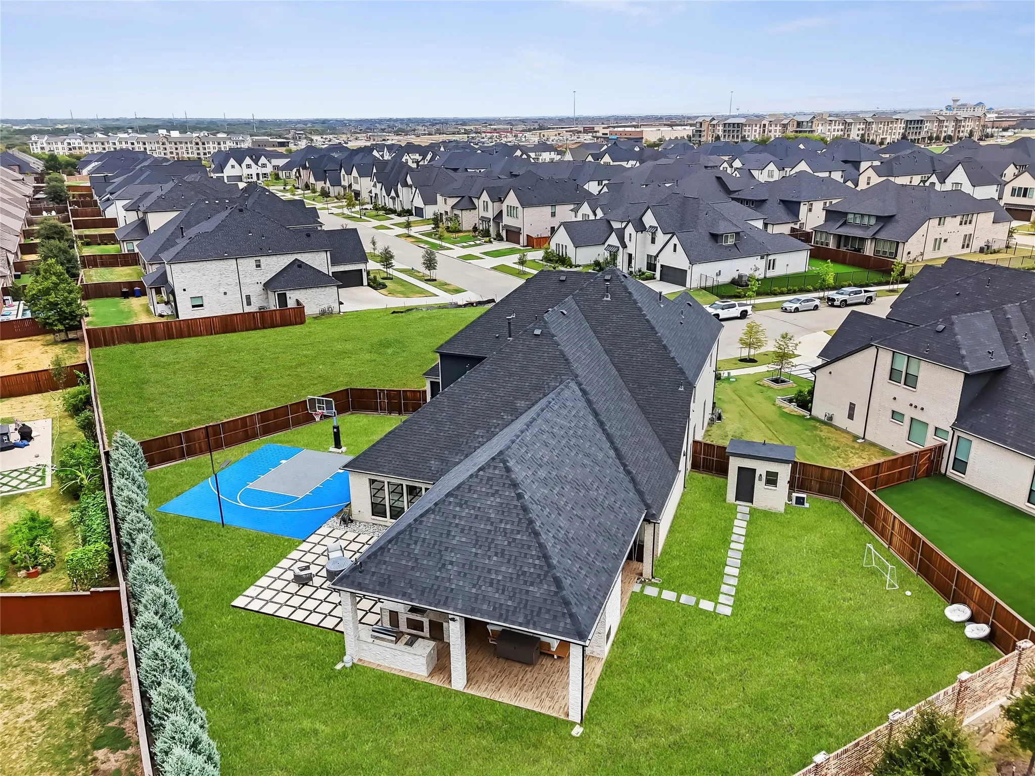 Expansive backyard featuring a manicured lawn, covered patio, sport court, and detached storage shed