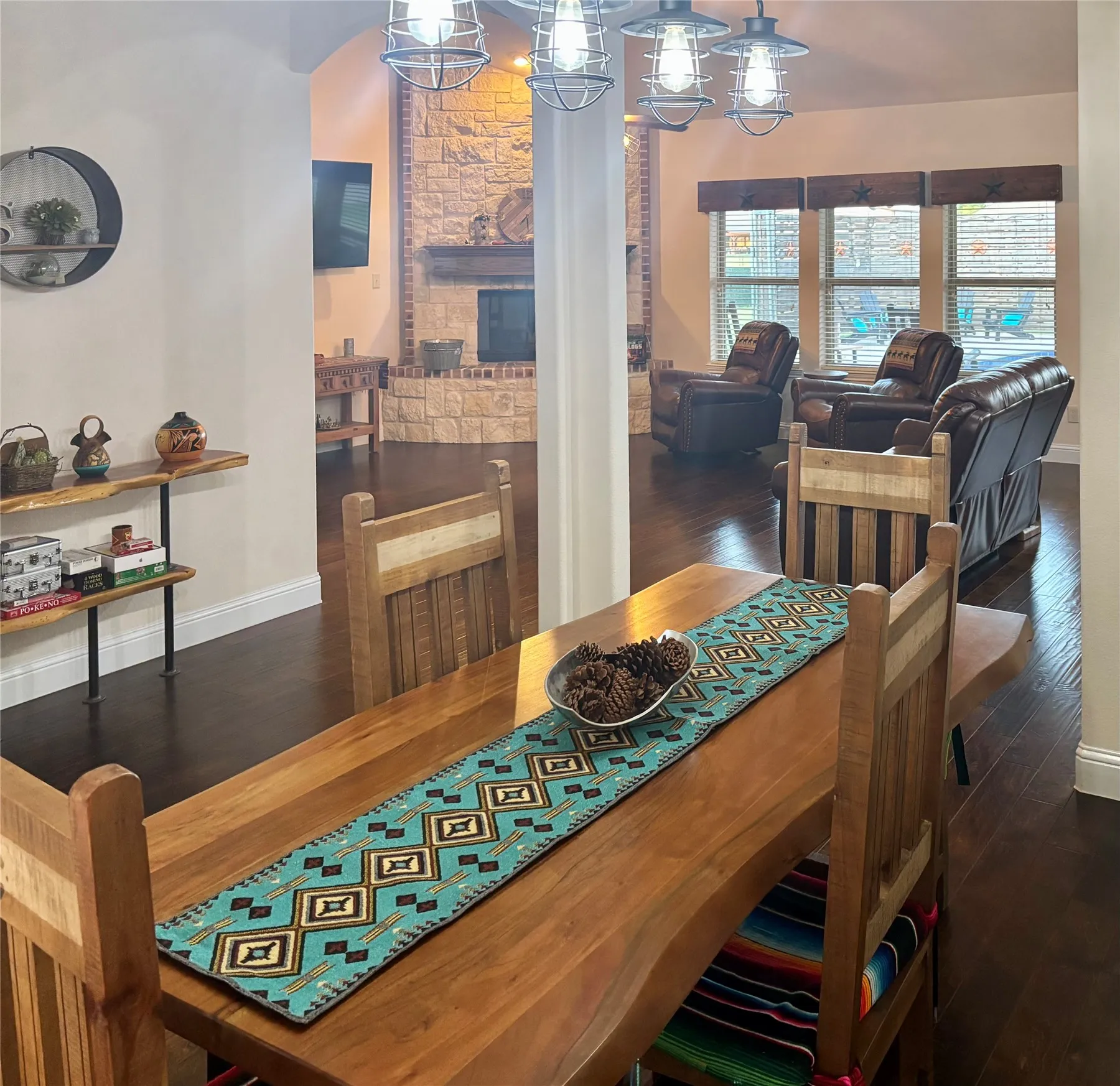 Wood-finish flooring, stone fireplace, arched entryway, exposed beam details, and ceiling-mounted lighting fixtures