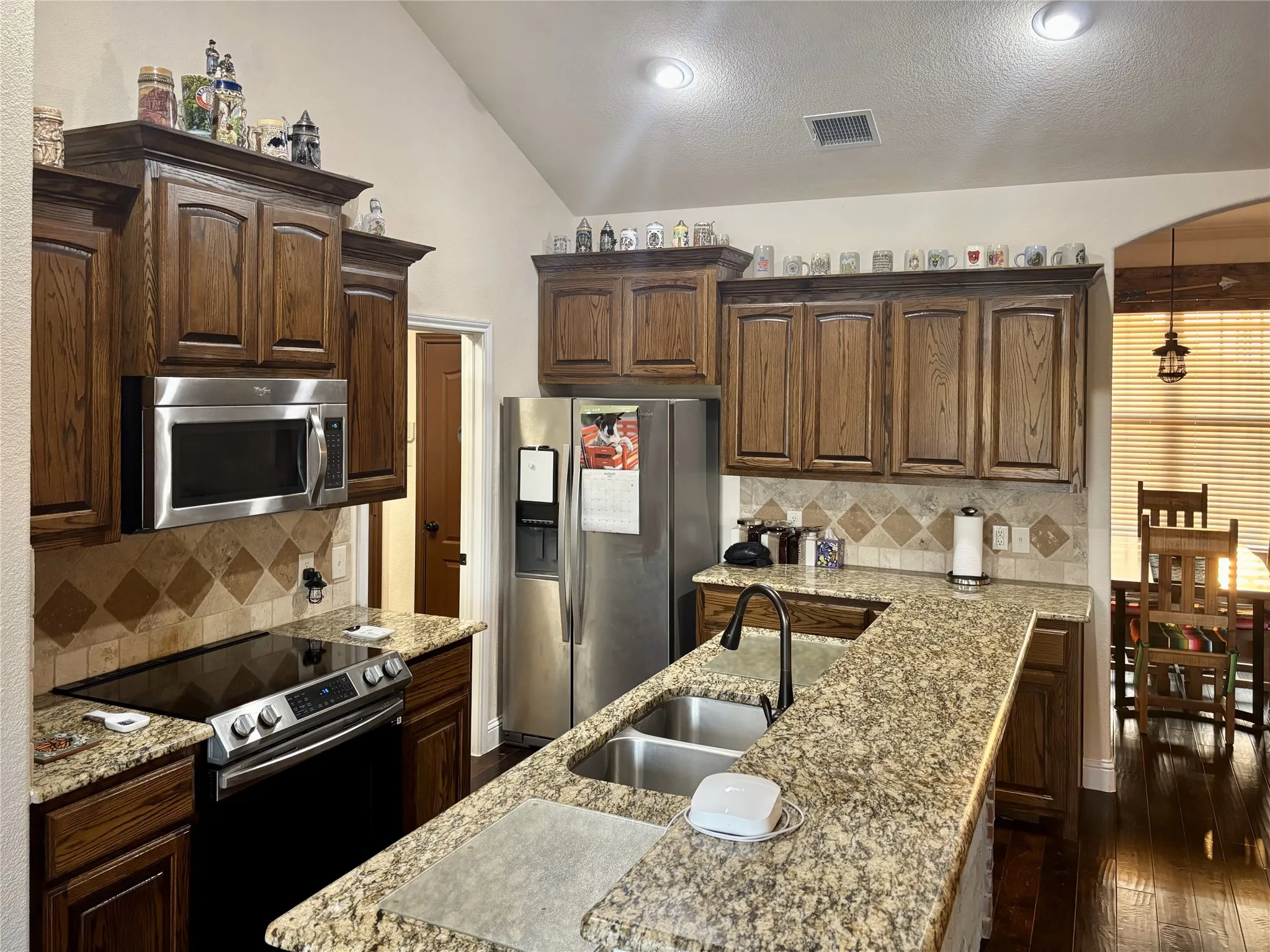 Kitchen featuring wood cabinetry, stainless steel appliances, granite countertops, tile backsplash, and recessed lighting
